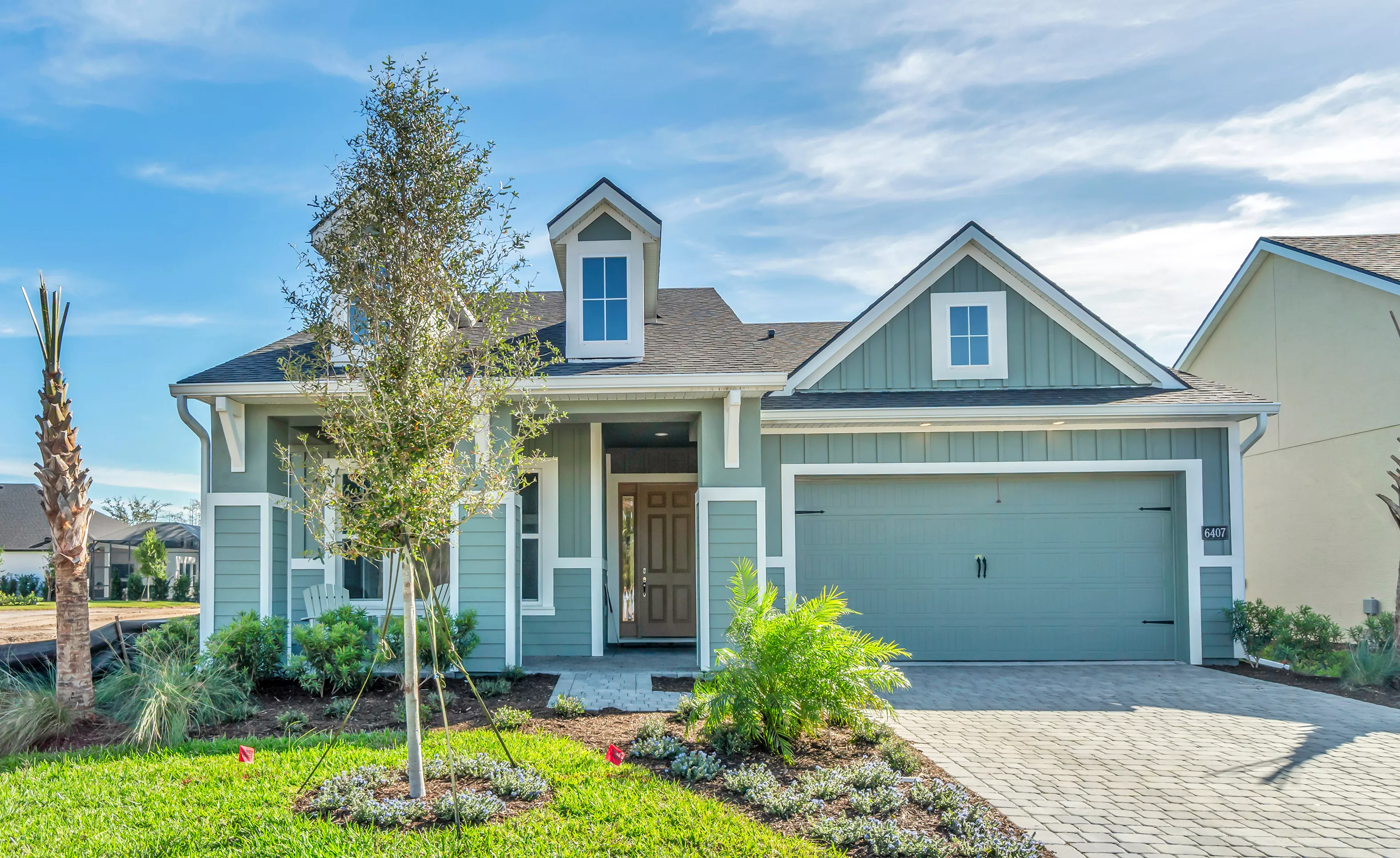 Front exterior of the Charlotte plan in Woodhaven, featuring light green siding, a two-car garage, and a central dormer.