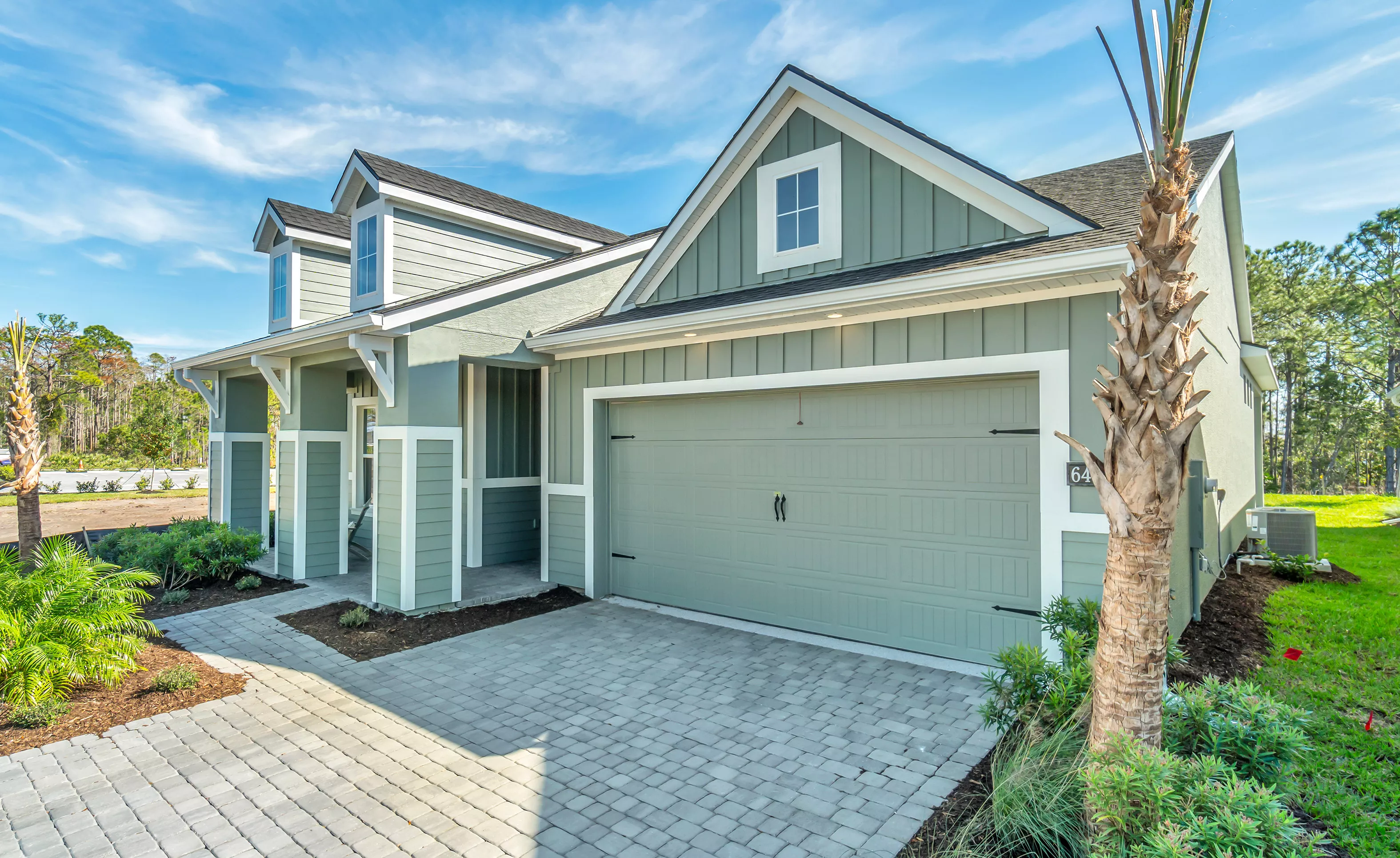 Front exterior of the Charlotte plan in Woodhaven featuring sage green siding, white trim, and a paved driveway.