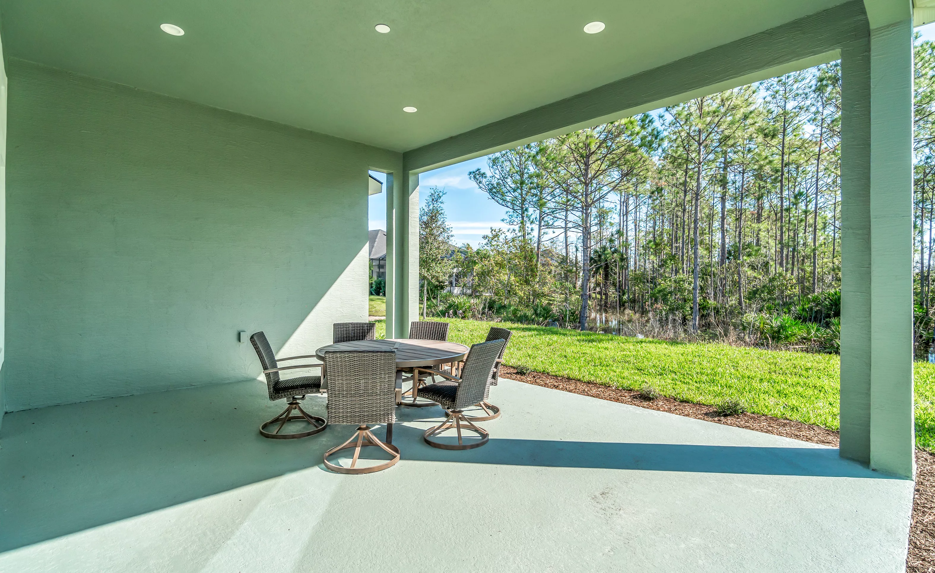 Covered porch of the Charlotte plan with recessed lighting, outdoor dining set, and a view of the backyard and woods.