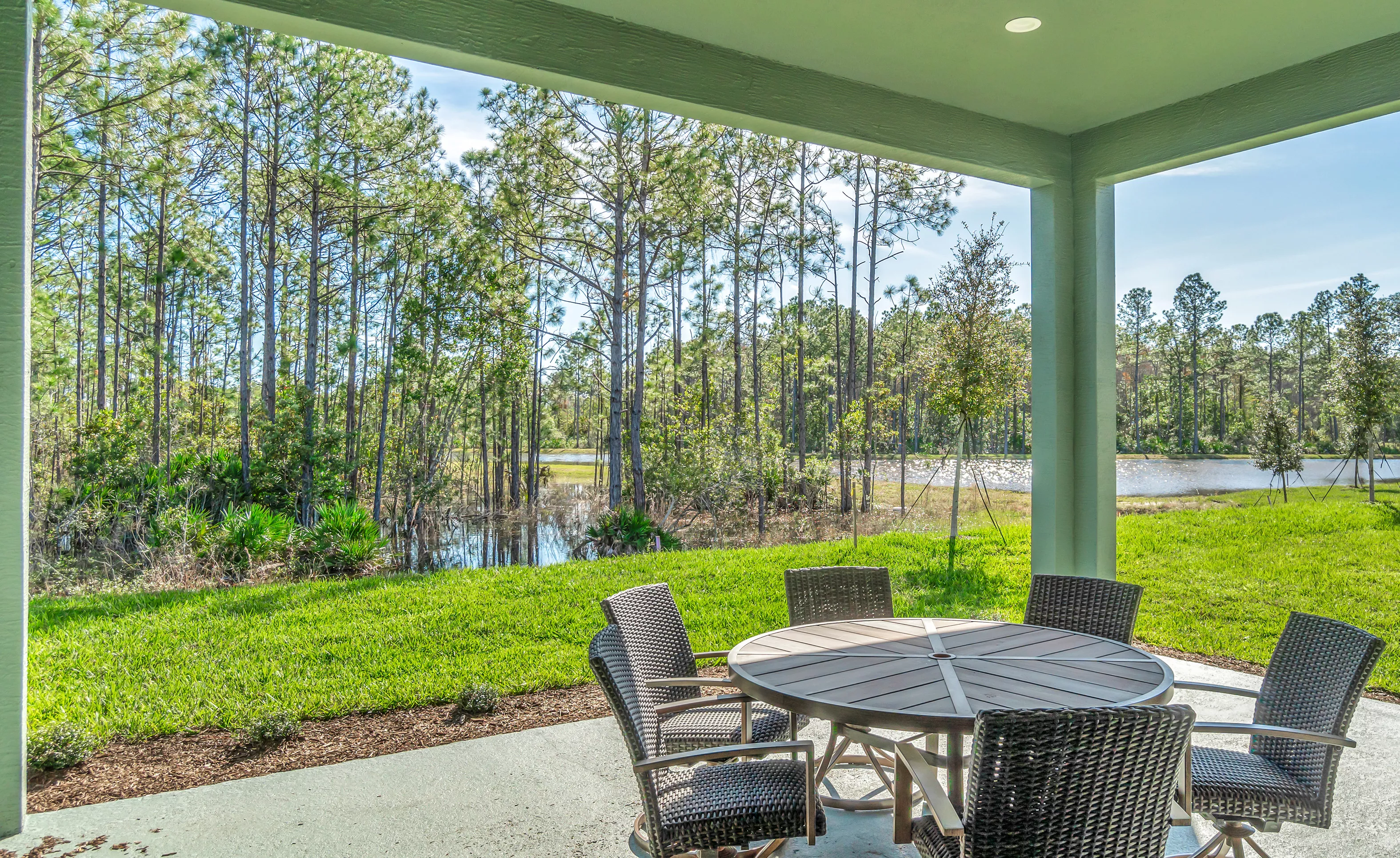 Charlotte plan covered porch in Woodhaven featuring outdoor table and chairs overlooking a wooded pond.