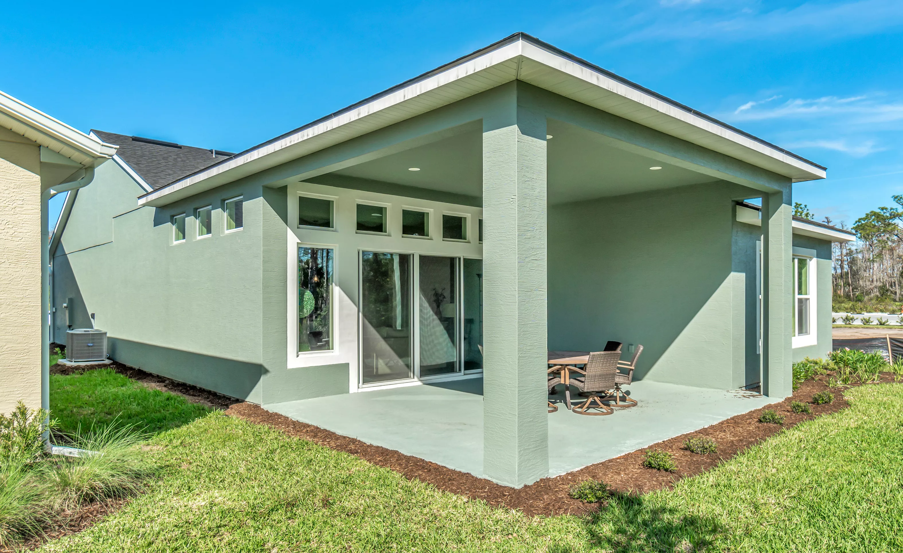 Covered back porch of a green stucco home with a concrete patio, sliding glass doors, and a small outdoor dining set.