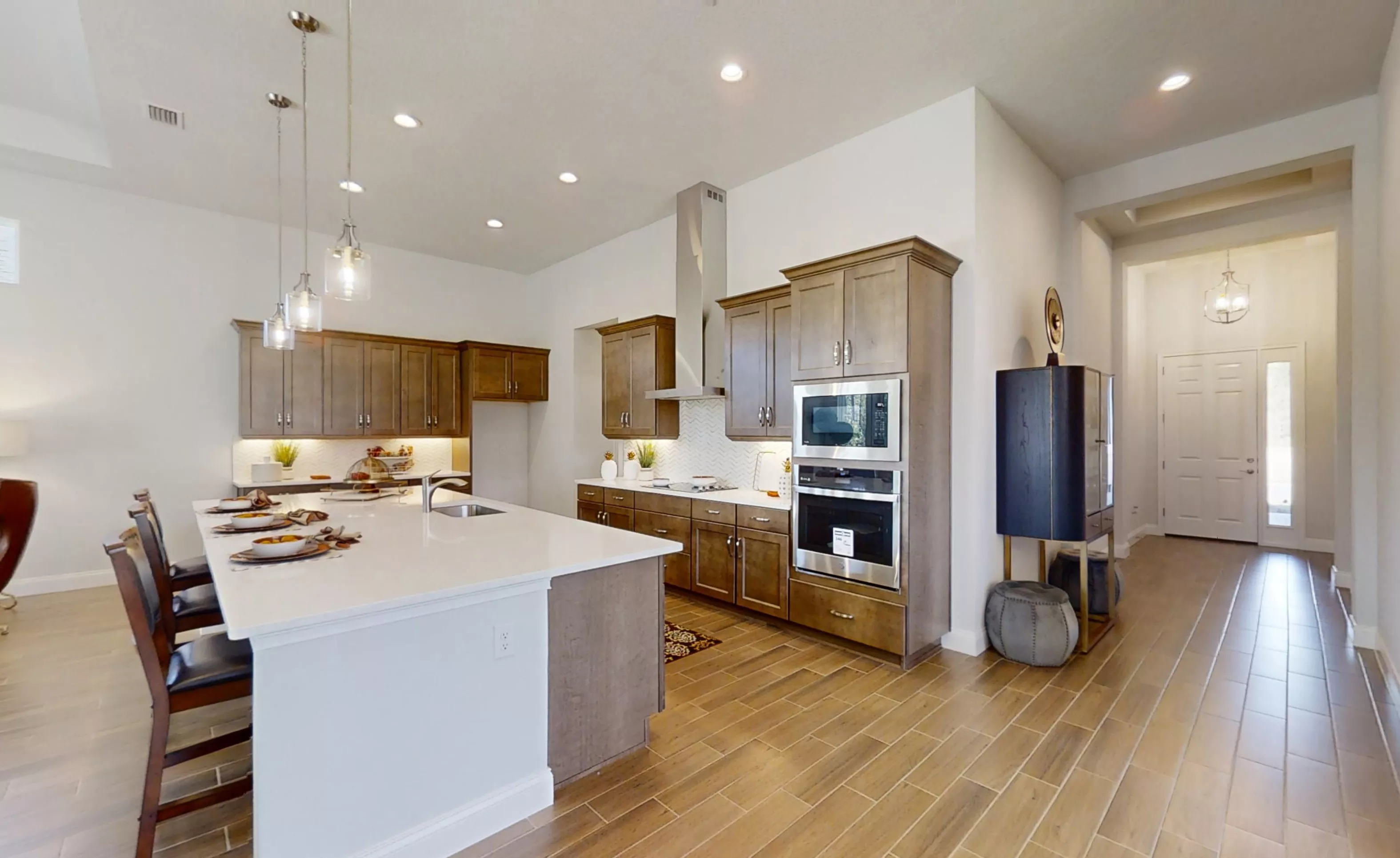 Charlotte plan kitchen with wood cabinets, white countertops, central island, stainless appliances, and wood-look tile floors.
