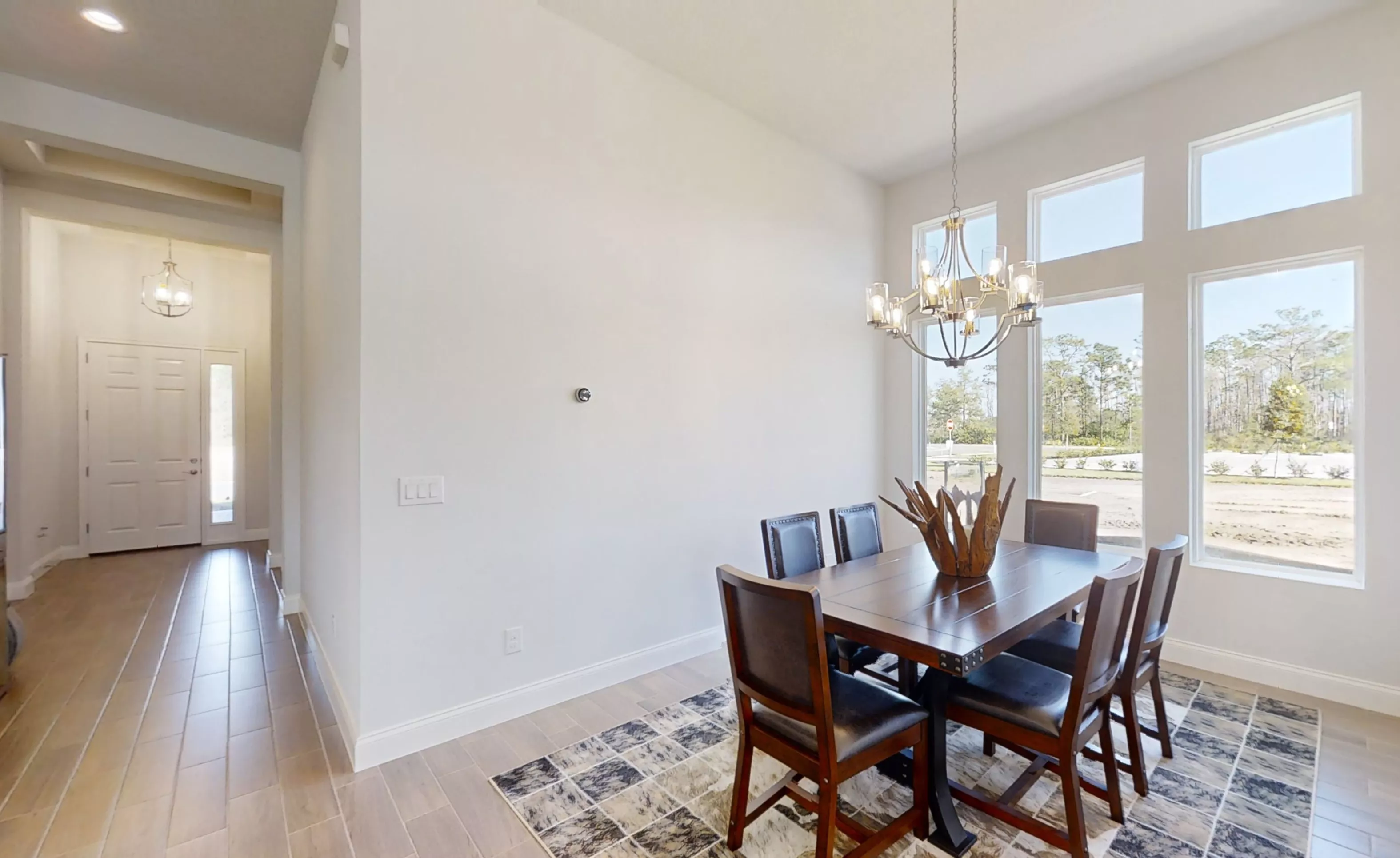 Dining room with dark wood table, six chairs, chandelier, tile floors, and large windows overlooking a construction site.