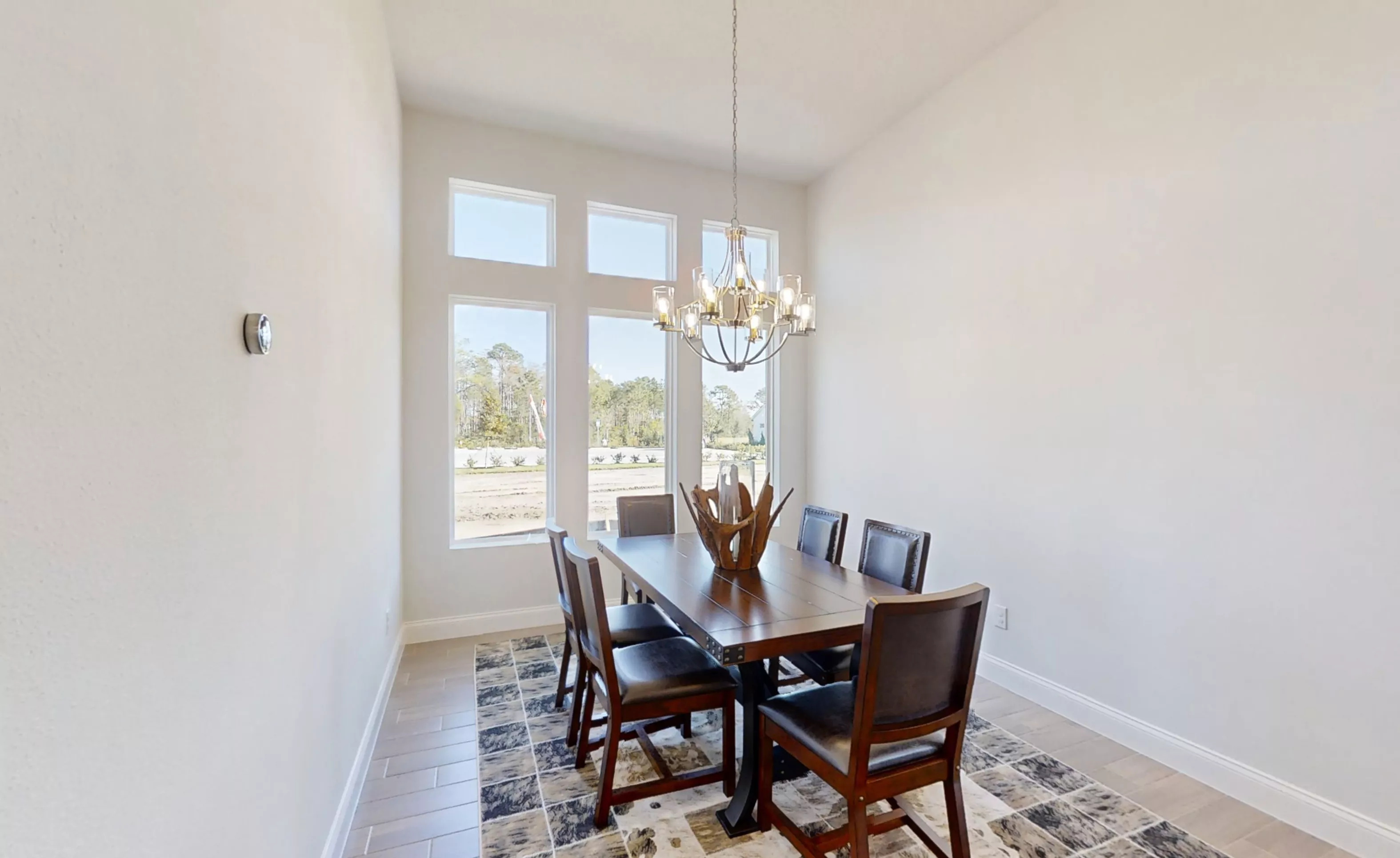 Dining room in the Charlotte floor plan with a dark wood table, six chairs, a chandelier, and tall windows.