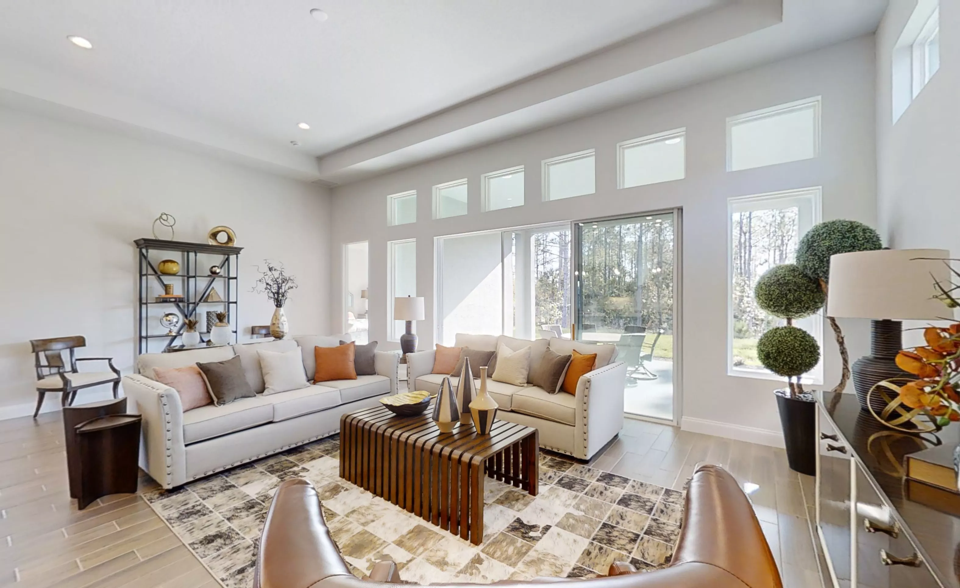 Living room of the Charlotte plan with tray ceiling, tile flooring, two sofas, and large windows with a glass patio door.