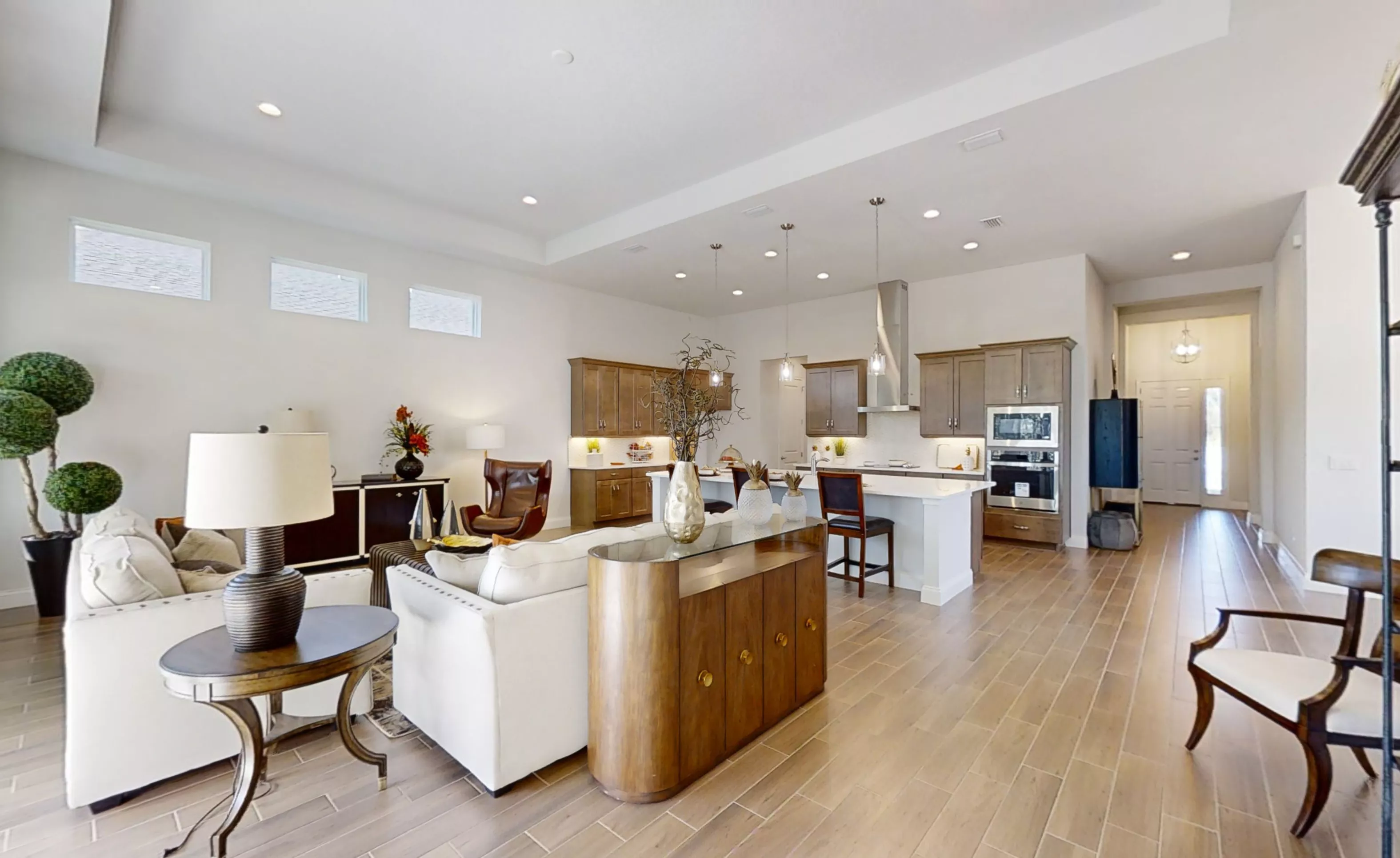 Charlotte plan living room with wood-look tile floors, an open kitchen with brown cabinets, and a white sofa.