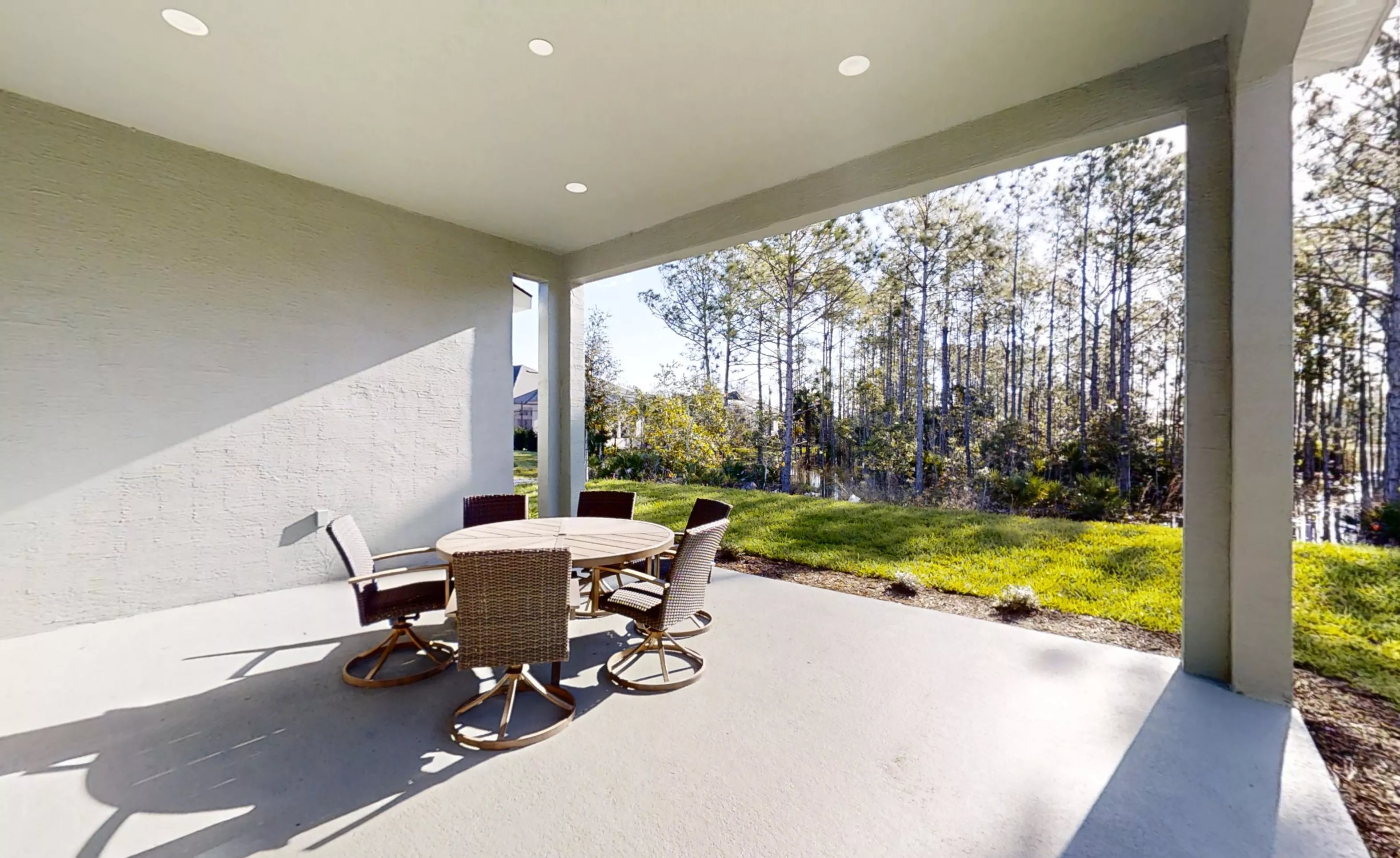 Covered porch with a round outdoor dining set overlooking a grassy lawn and a wooded area.