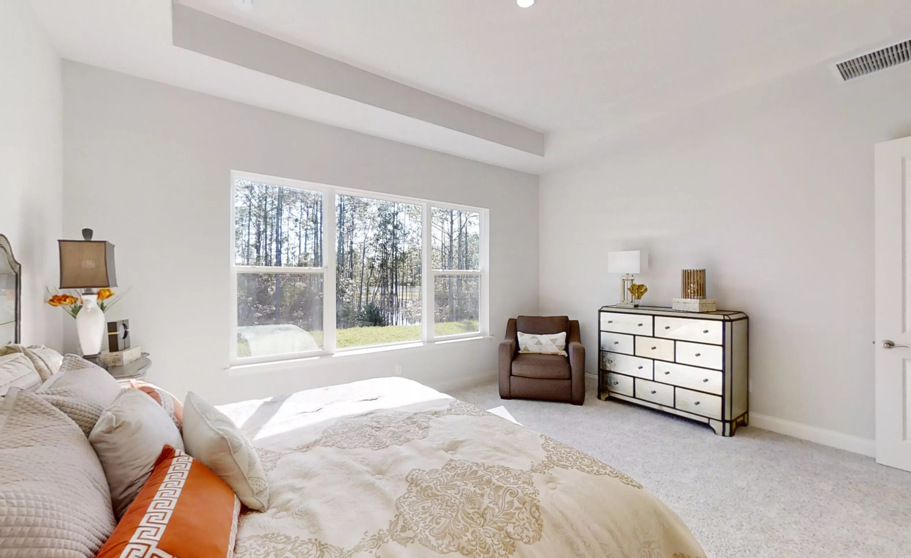 Primary bedroom in the Charlotte plan with light walls, tray ceiling, carpet, and a large window overlooking a wooded area.