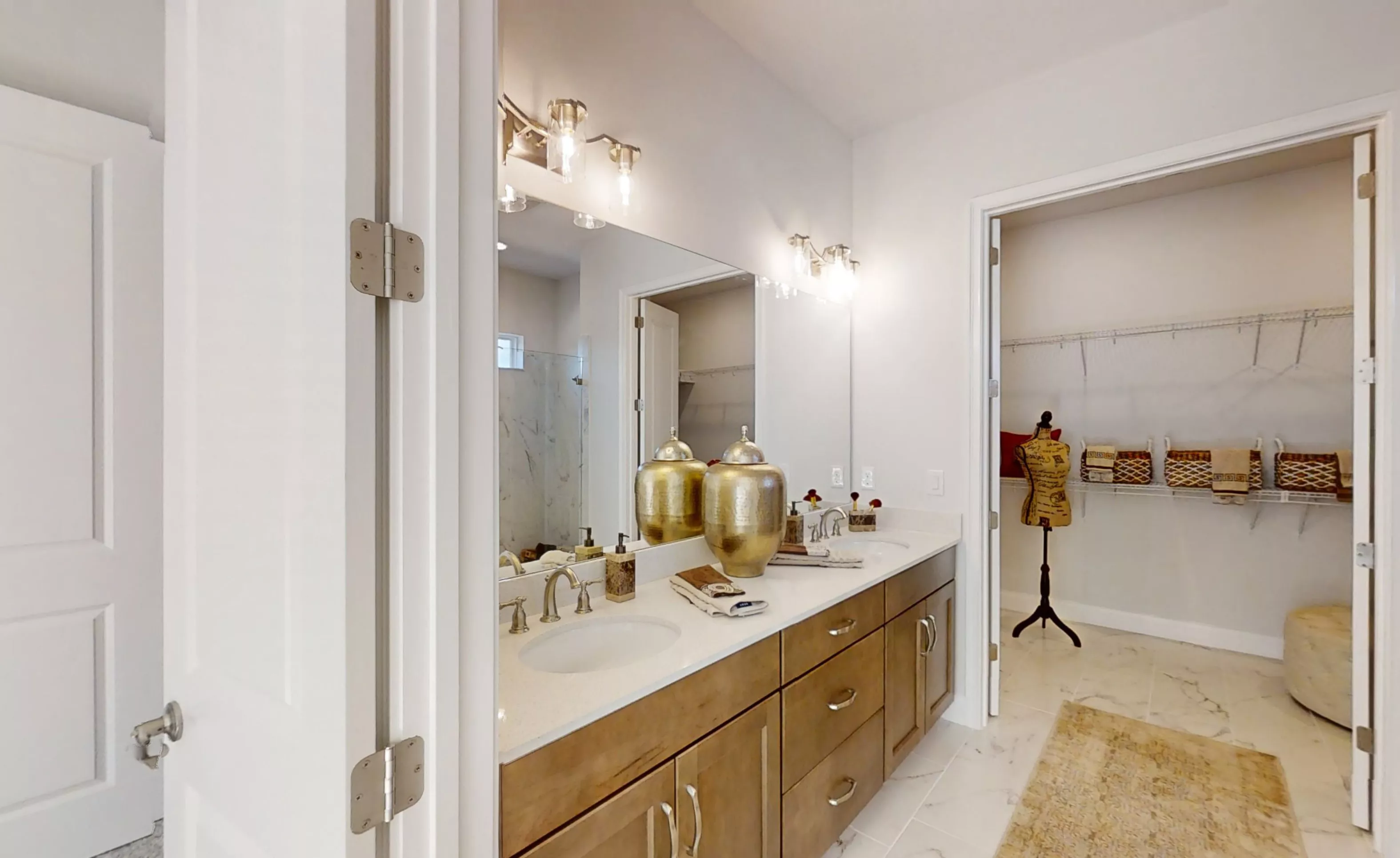 Primary bath in the Charlotte plan featuring a double vanity with wood cabinets, light countertops, and a walk-in closet.