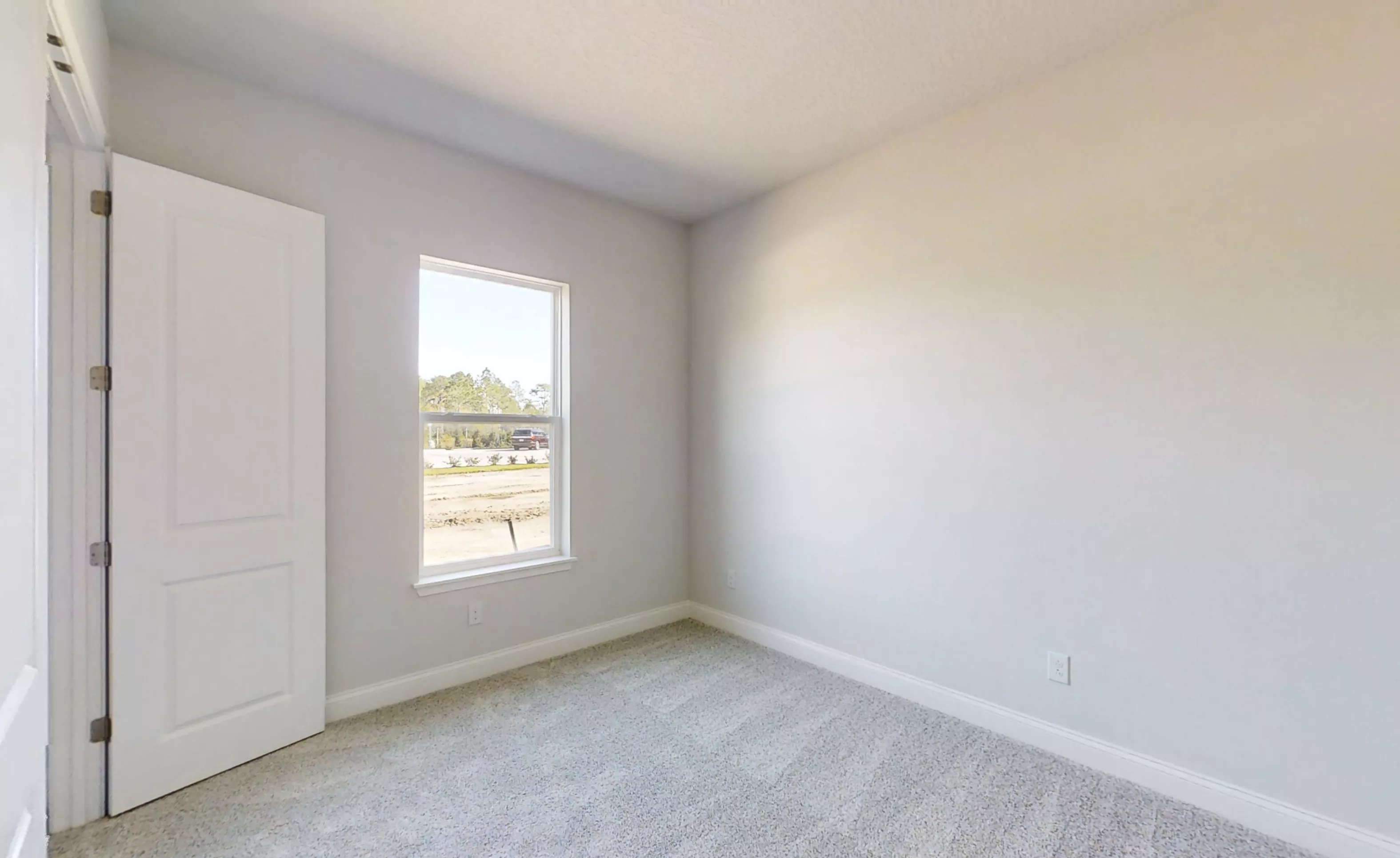 Empty secondary bedroom with light gray walls, white trim, carpeted flooring, and a window overlooking a construction site.