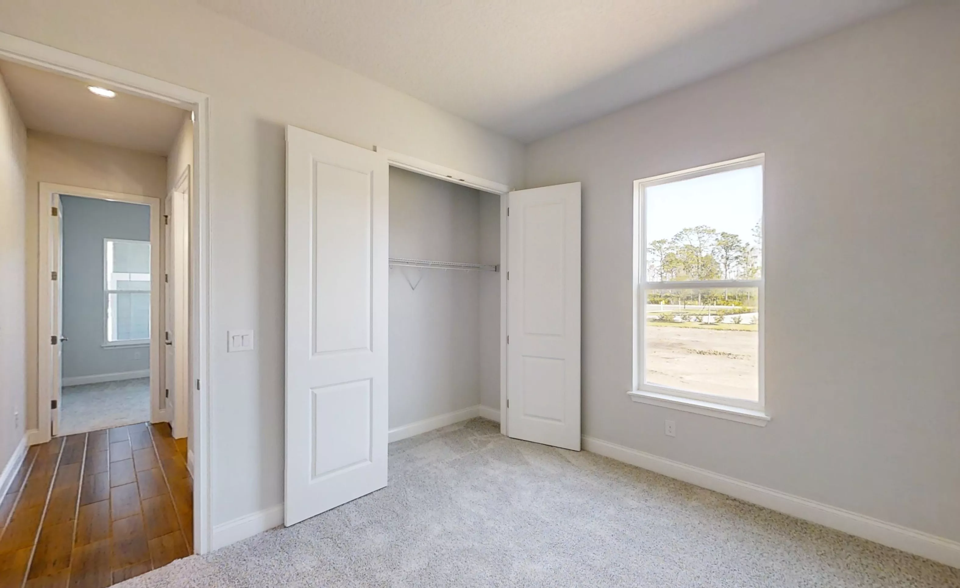 Secondary bedroom with light gray walls, carpeted floor, open closet, and a window looking out to a landscaped yard.