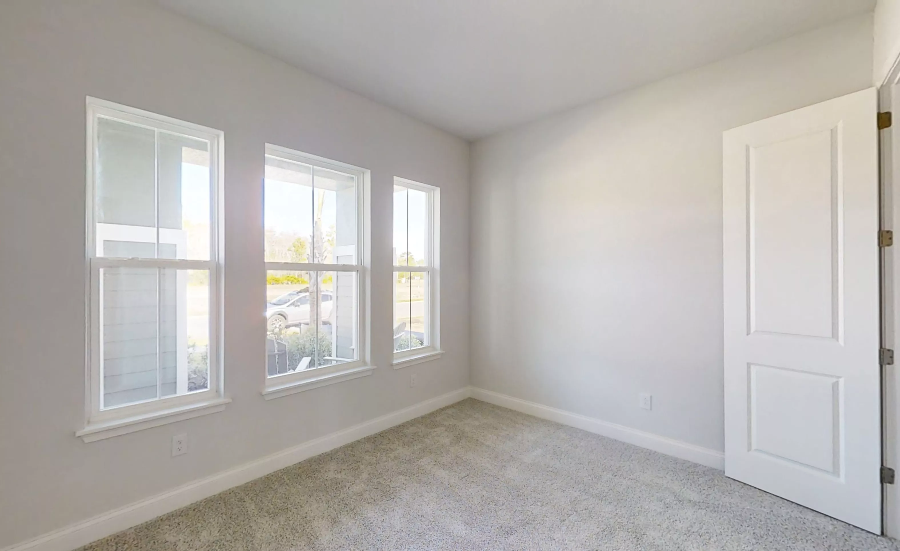 Secondary bedroom with gray carpet, light gray walls, three tall windows, and a white interior door.