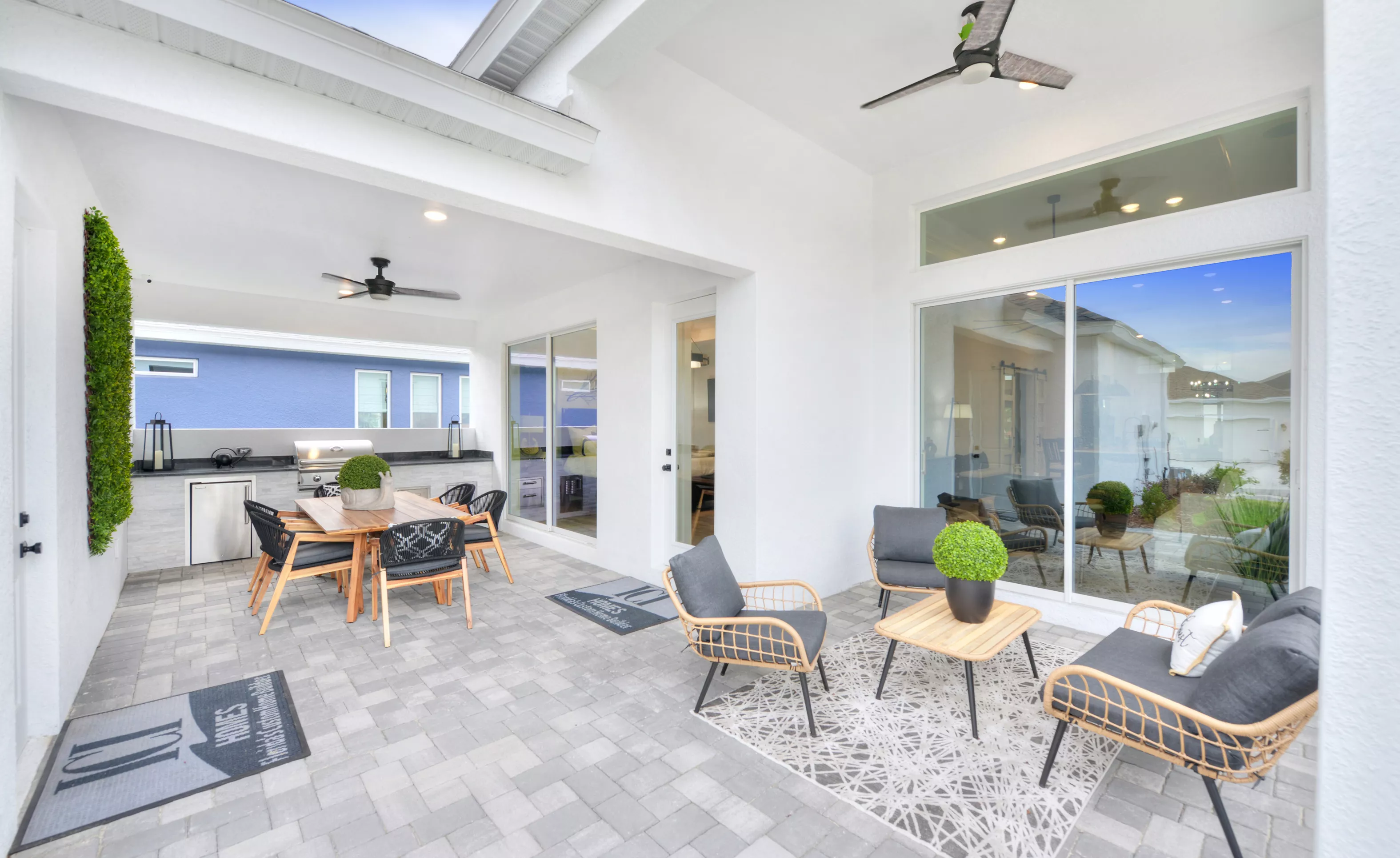 Covered lanai with a paver floor, outdoor dining area with a grill, and a separate seating area with modern patio furniture.