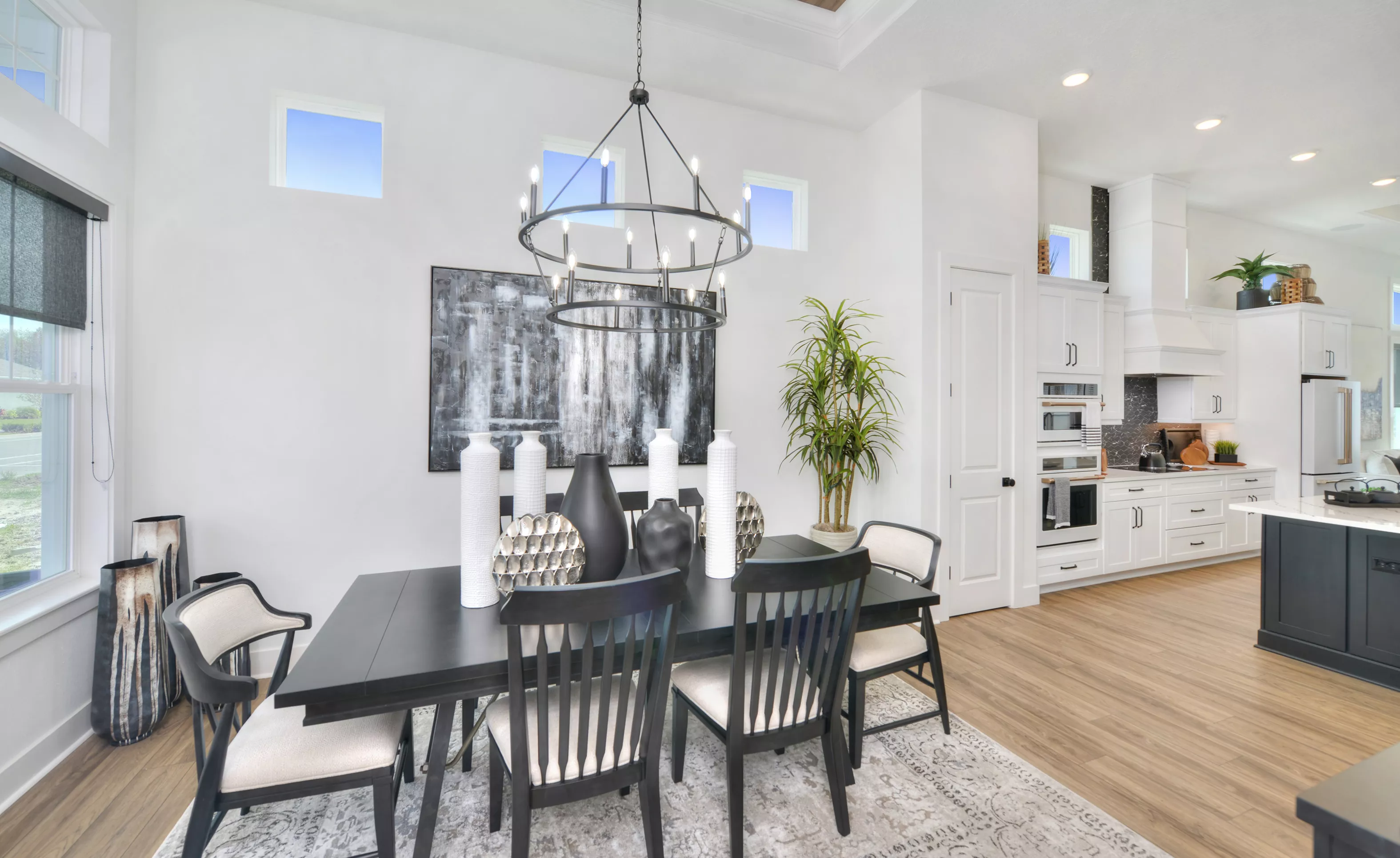 Dining room in the Lantana plan with a black table, chairs, modern chandelier, and a view into the adjacent white kitchen.