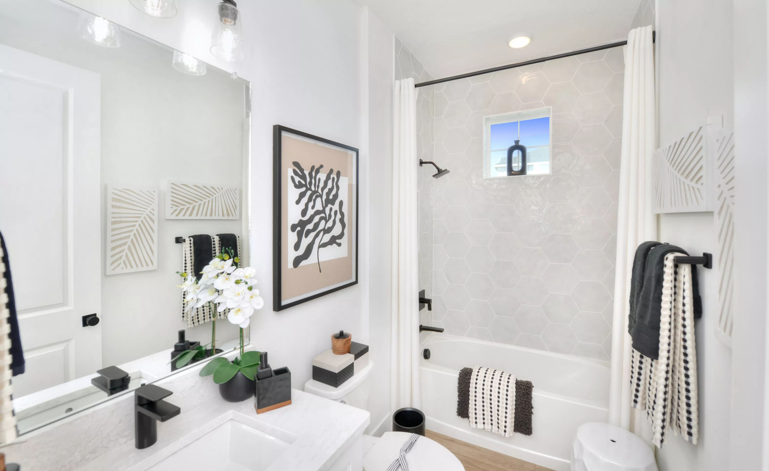 Secondary bath with white vanity, large mirror, black fixtures, and a tub-shower with gray hexagonal wall tiles.