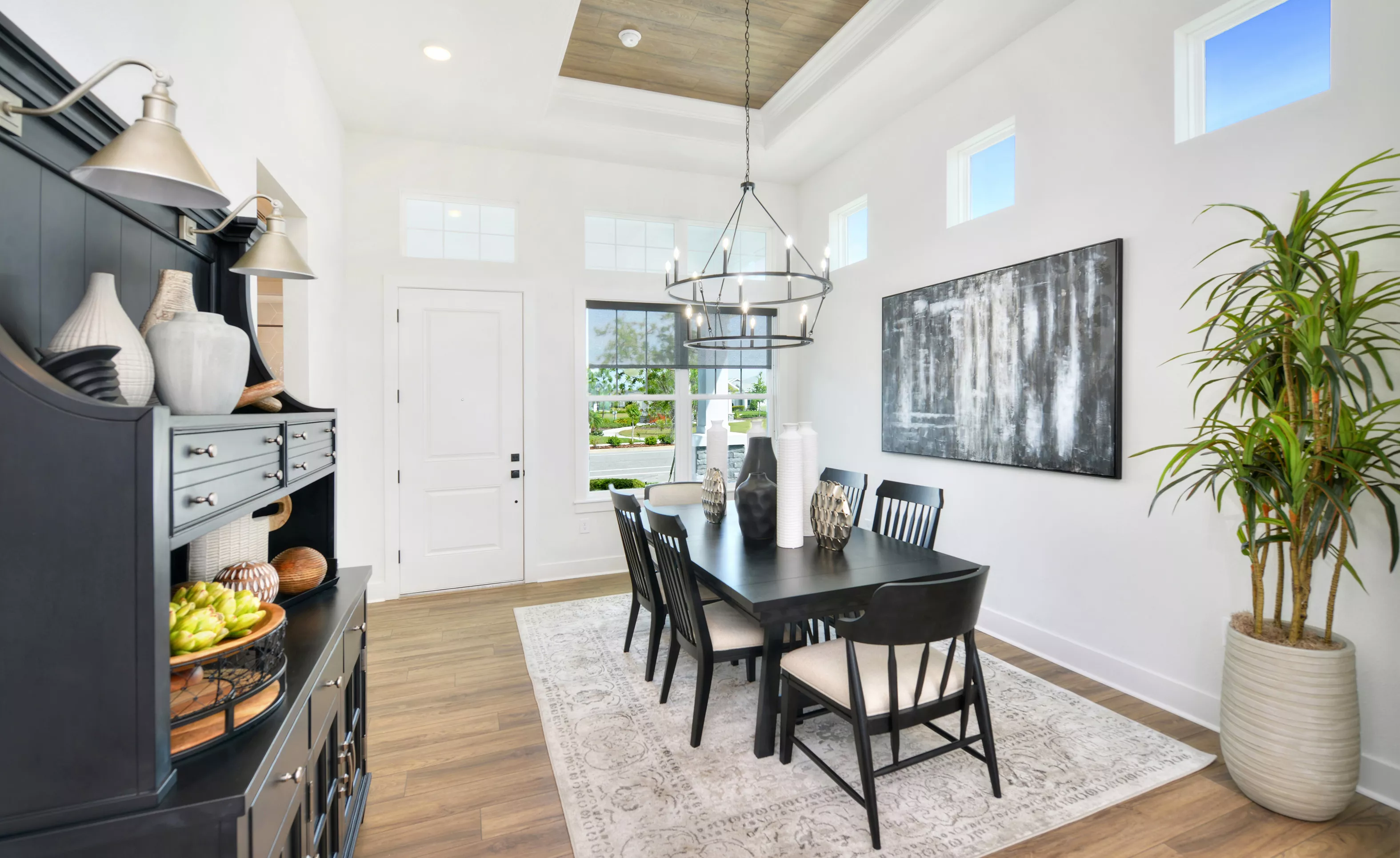 Dining room in the Lantana plan with a wood-accented tray ceiling, black dining set, chandelier, and a large wall painting.