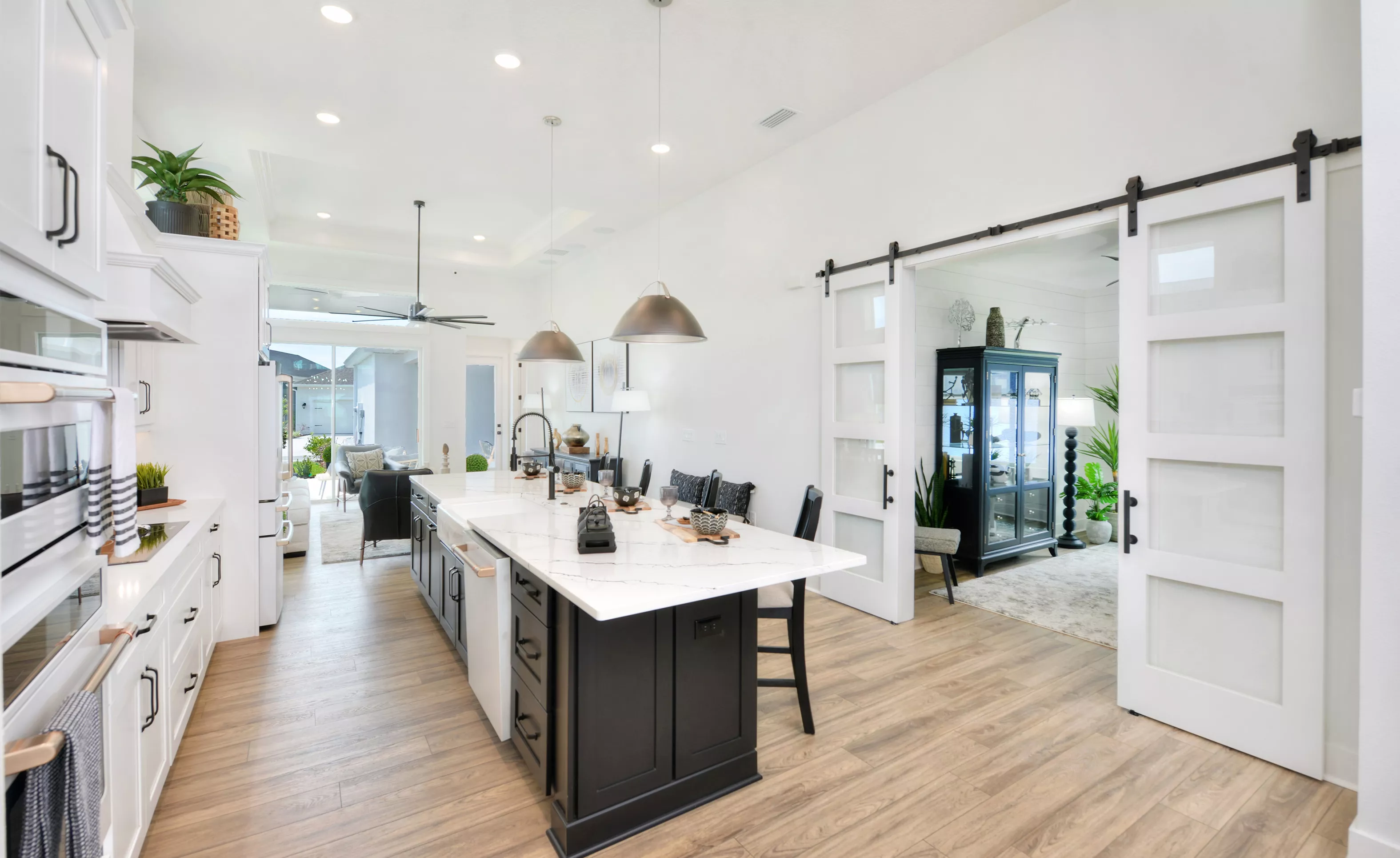 Lantana plan kitchen with a large dark island, white marble-look countertops, and white barn doors opening to a den.