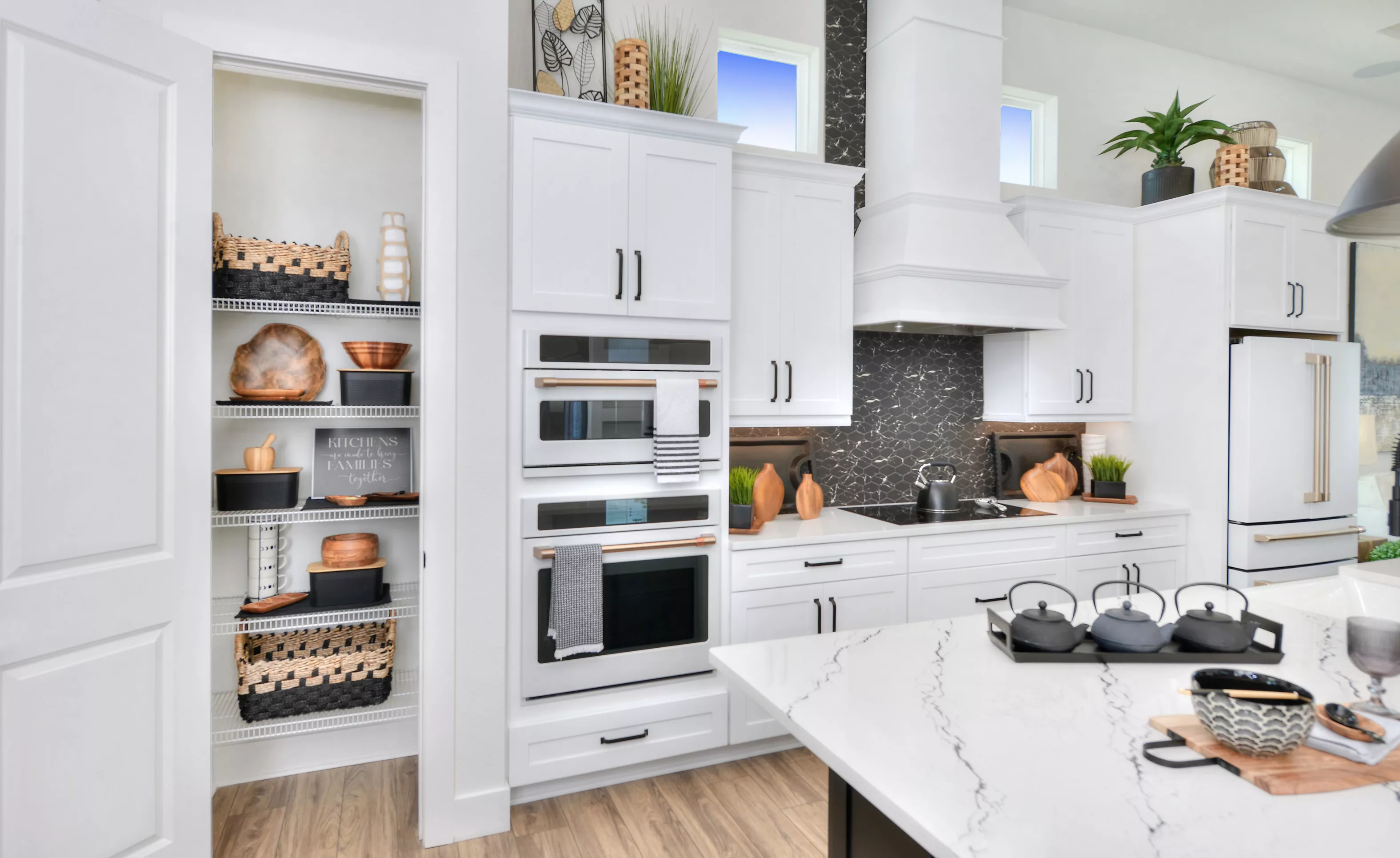 Lantana plan kitchen with white cabinets, double wall ovens, a black hexagonal tile backsplash, and a white marble island.