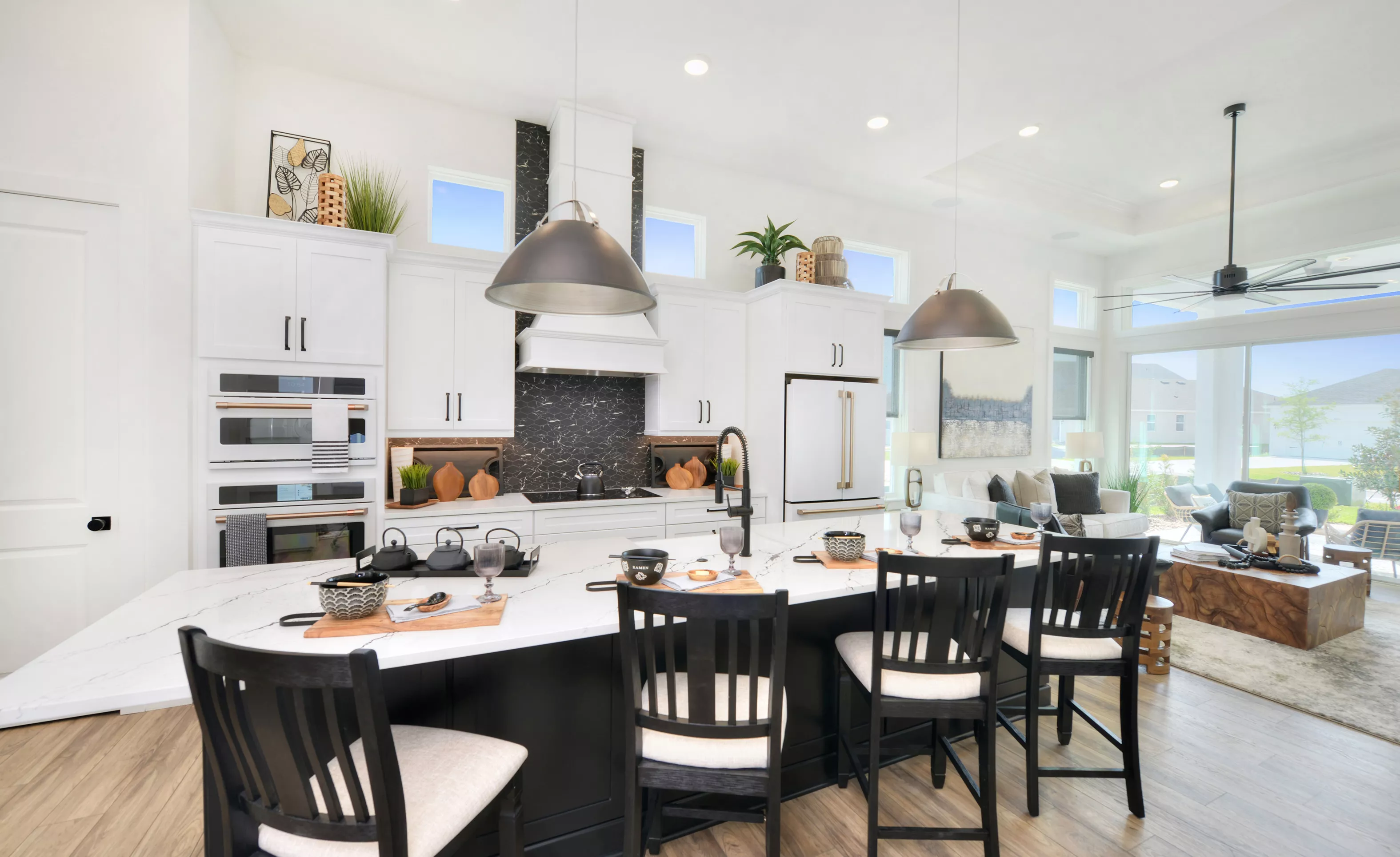 Lantana plan kitchen with white cabinets, marble-patterned island, black backsplash, and dark stools in an open floor plan.