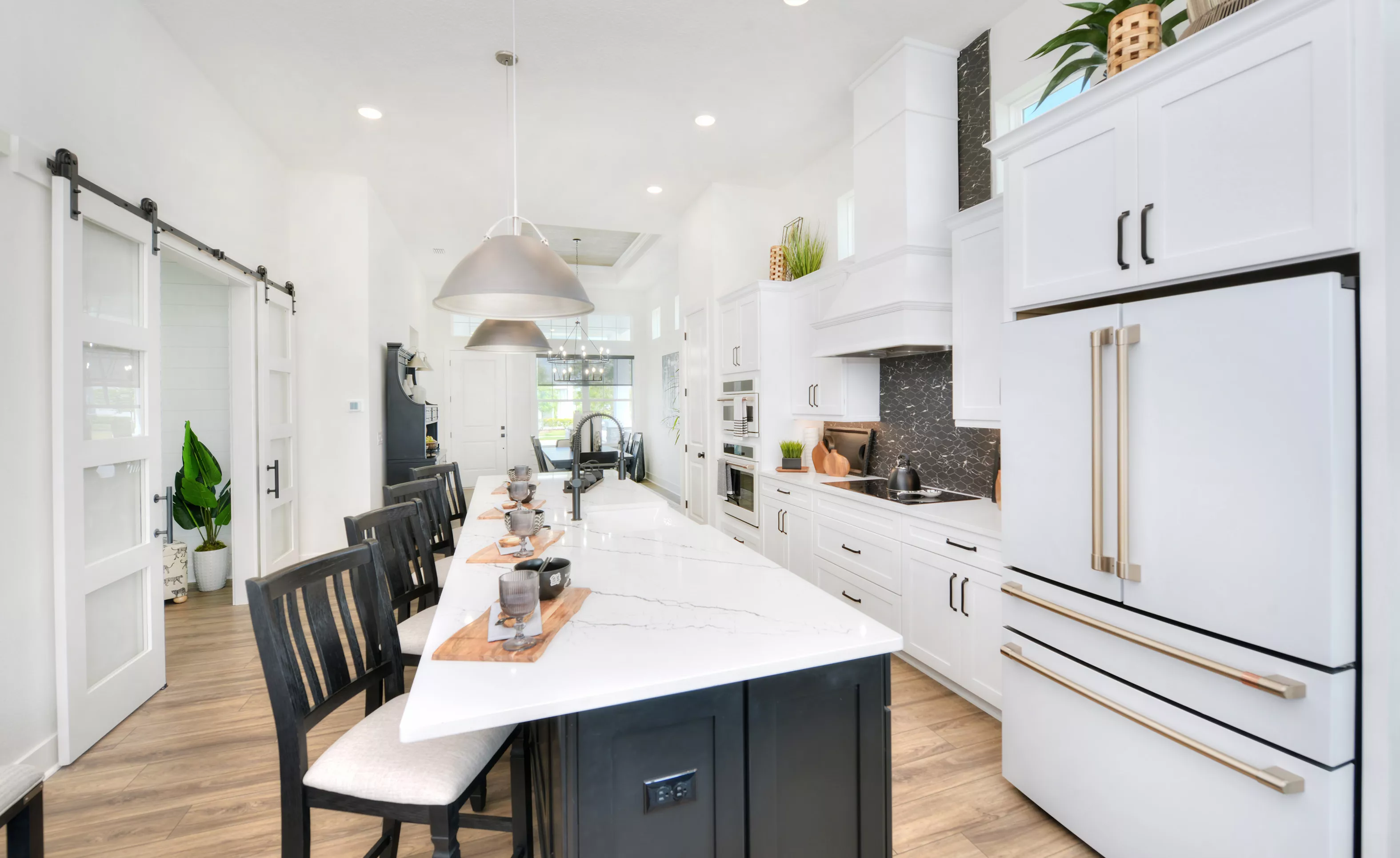 Lantana plan kitchen with a black island, white marble countertops, white cabinets, and a black patterned backsplash.