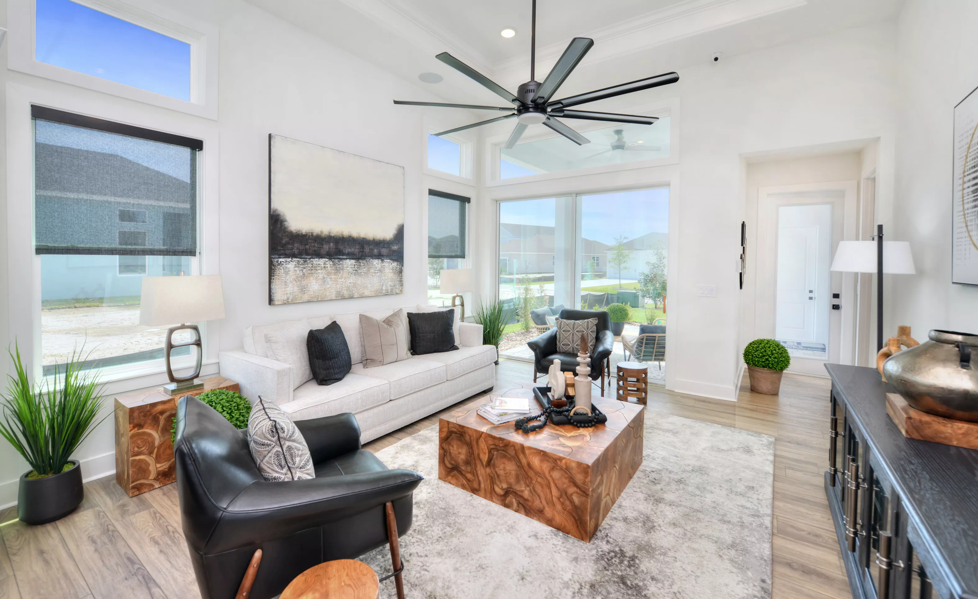 Living room in the Lantana floor plan with a white sofa, leather chairs, a wooden block coffee table, and large windows.