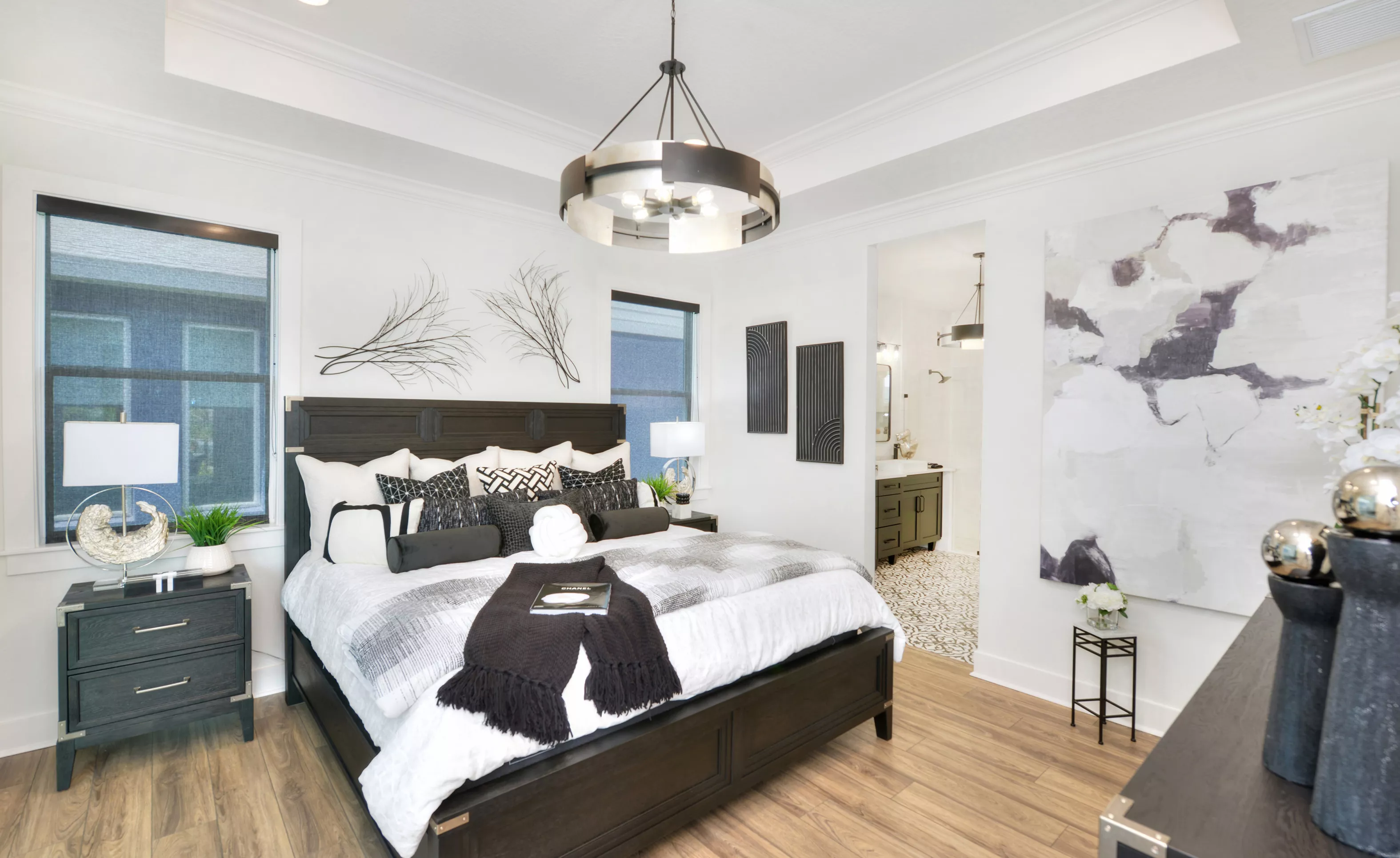 Primary bedroom in the Lantana plan with tray ceiling, dark wood furniture, and a view into the tiled primary bathroom.