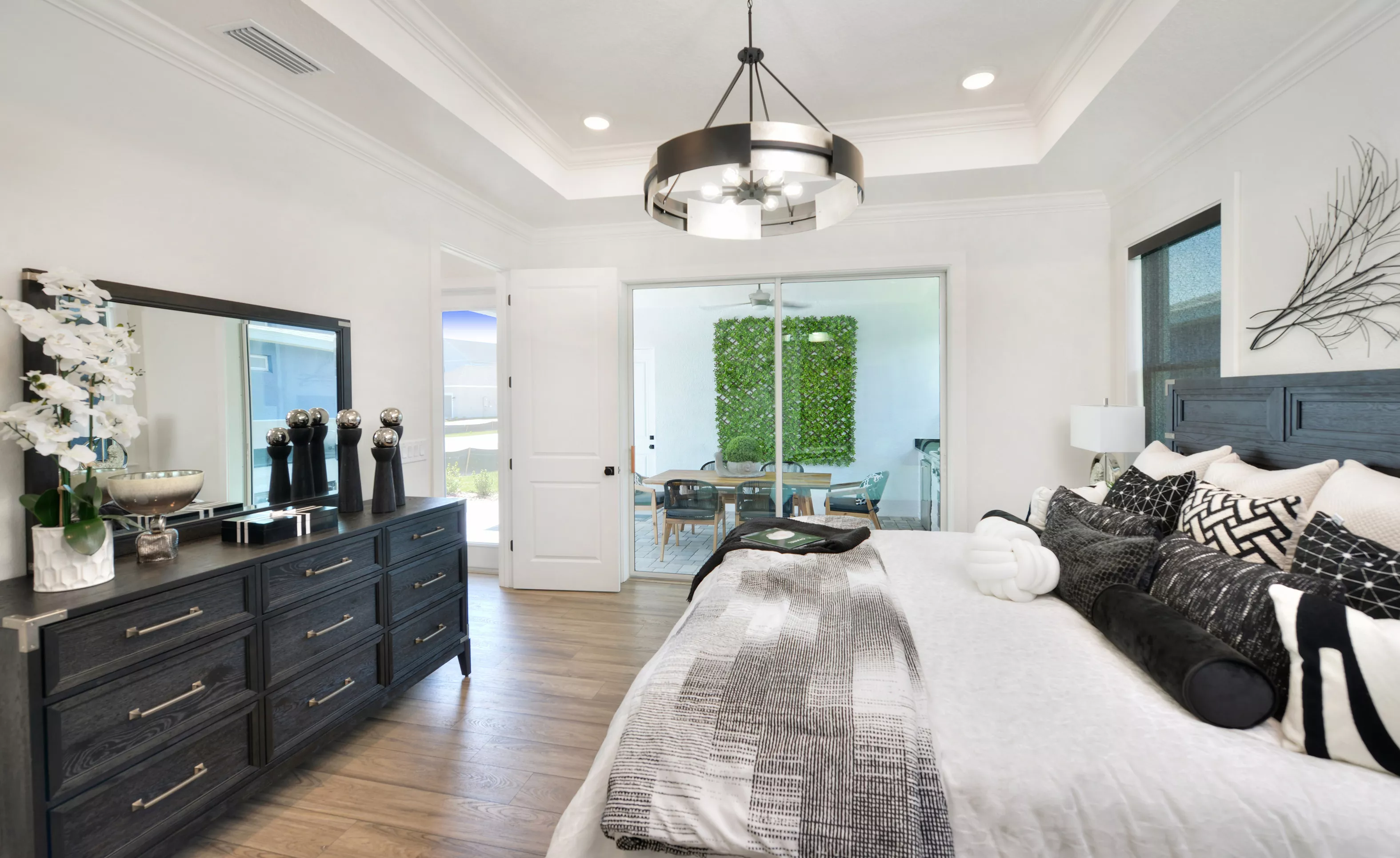 Primary bedroom with a king bed, dark wood dresser, tray ceiling, and sliding glass doors leading to a covered patio.