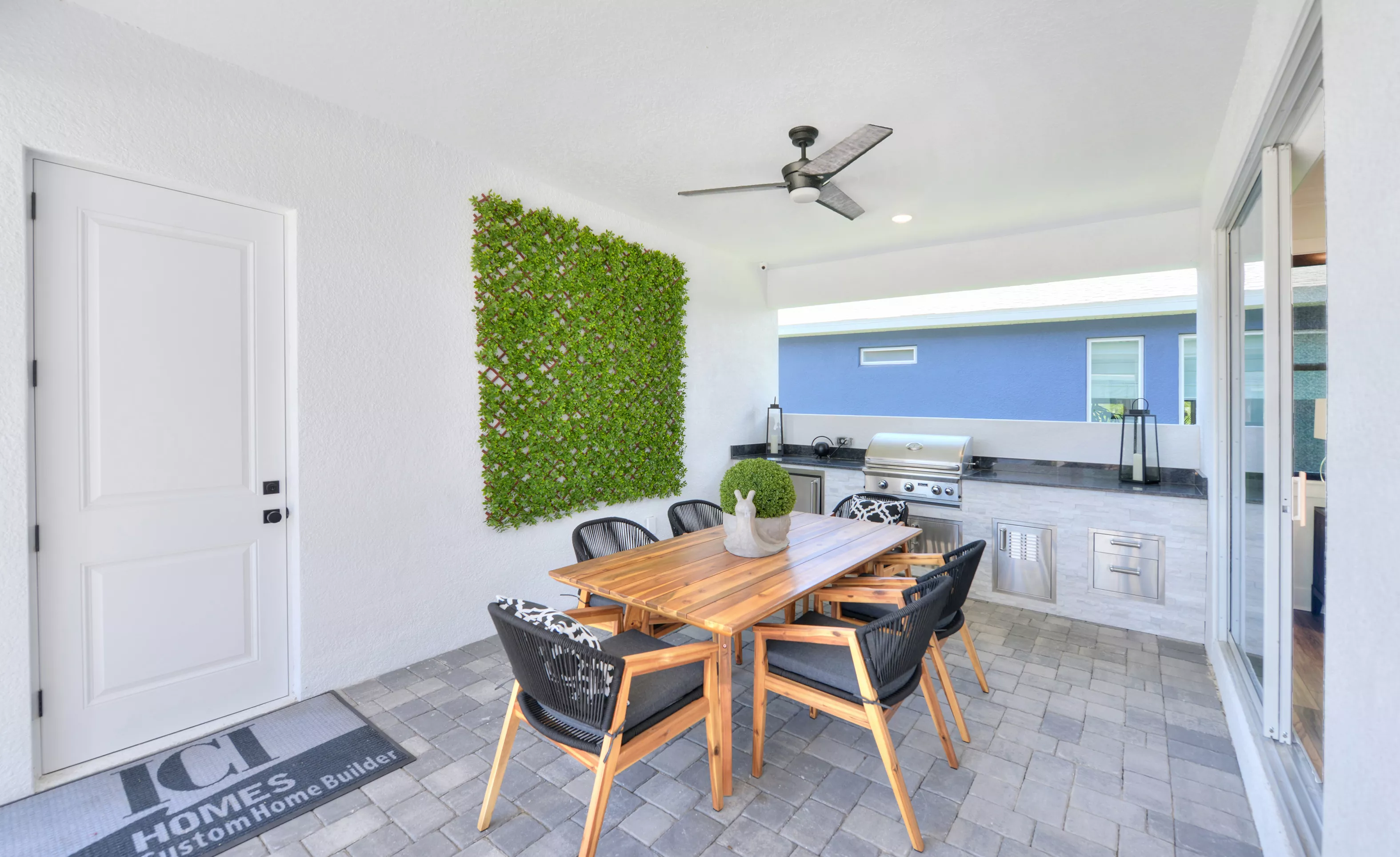 Lantana outdoor living space featuring a wood dining table, black chairs, a stone grill station, and a green wall trellis.