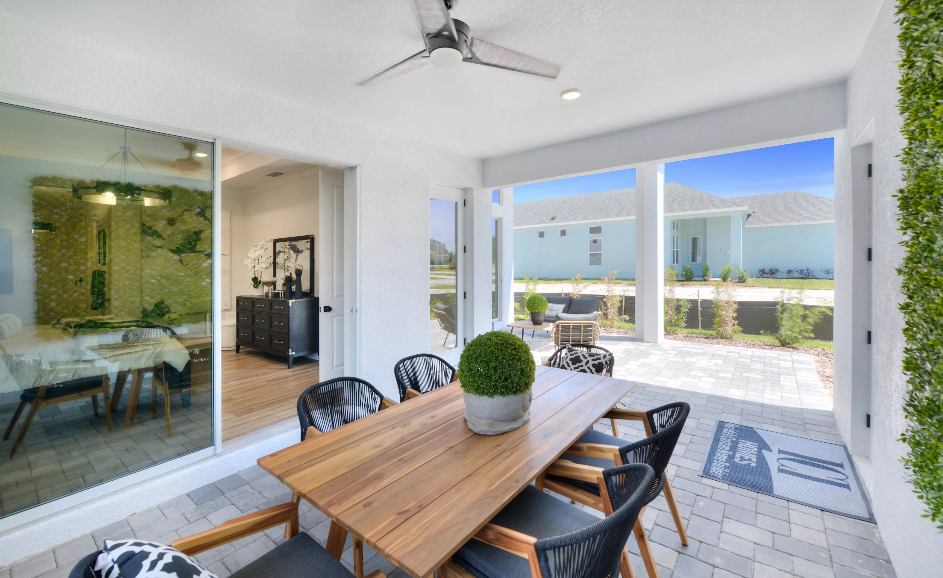 Covered lanai of the Lantana model featuring a wooden dining set, paved floor, ceiling fan, and view of the backyard.