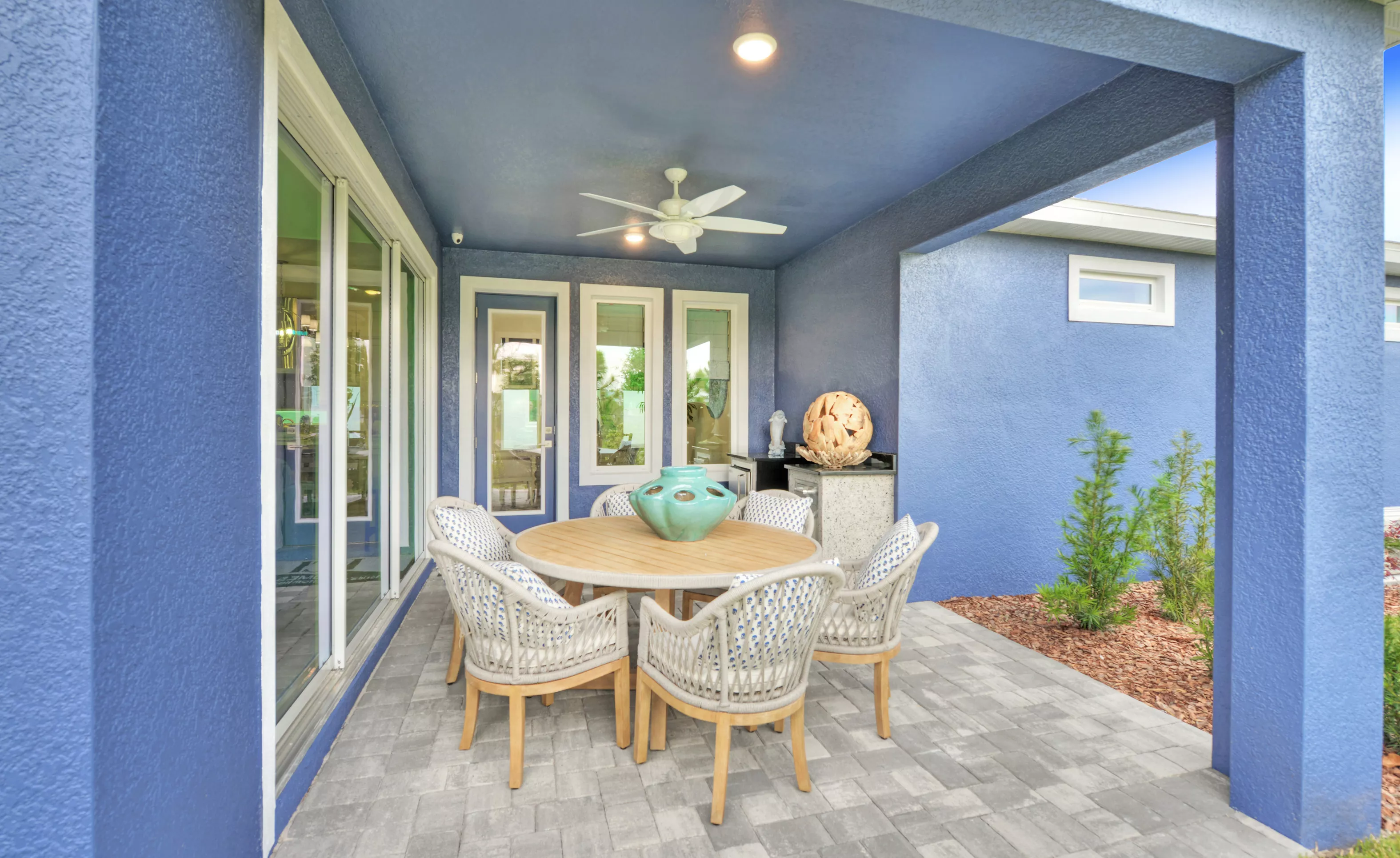 Covered lanai of the Azalea plan with blue stucco walls, paver flooring, outdoor dining set, and small kitchenette.