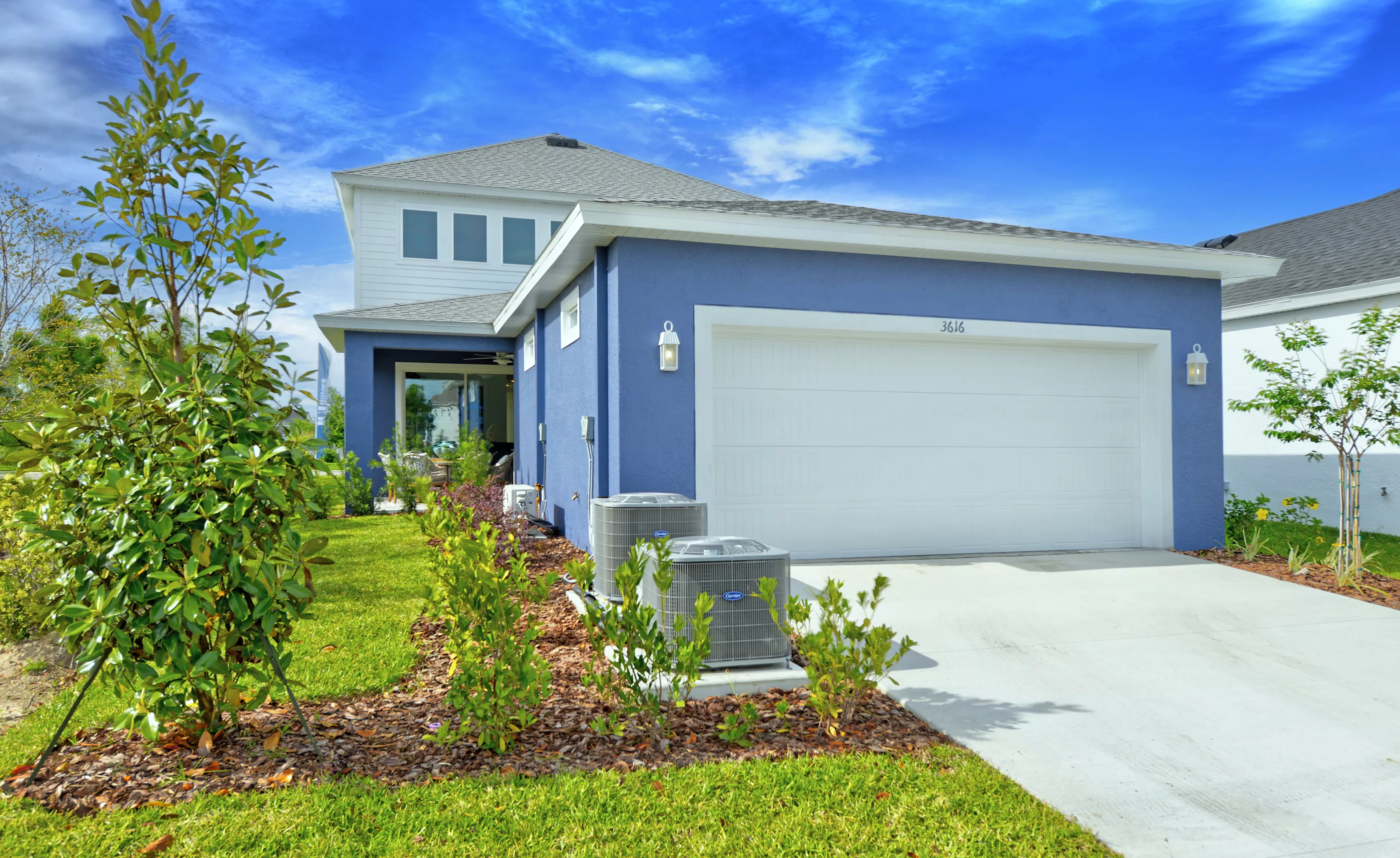 Side exterior view of a blue Azalea model home in Persimmon Park, featuring a two-car garage, lawn, and AC units.