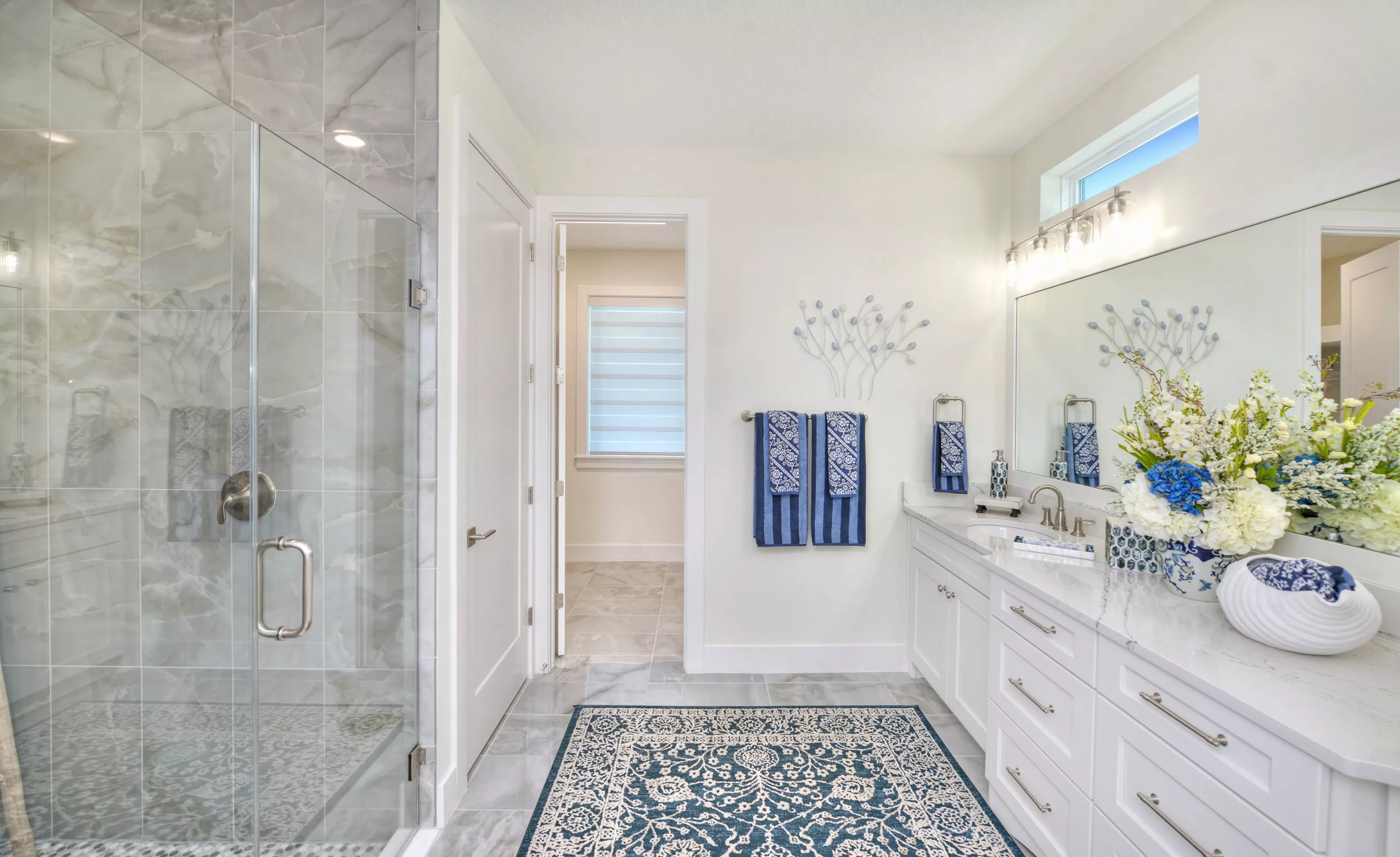 Primary bath with a glass-enclosed shower, white vanity with marble countertop, and a doorway leading to a walk-in closet.