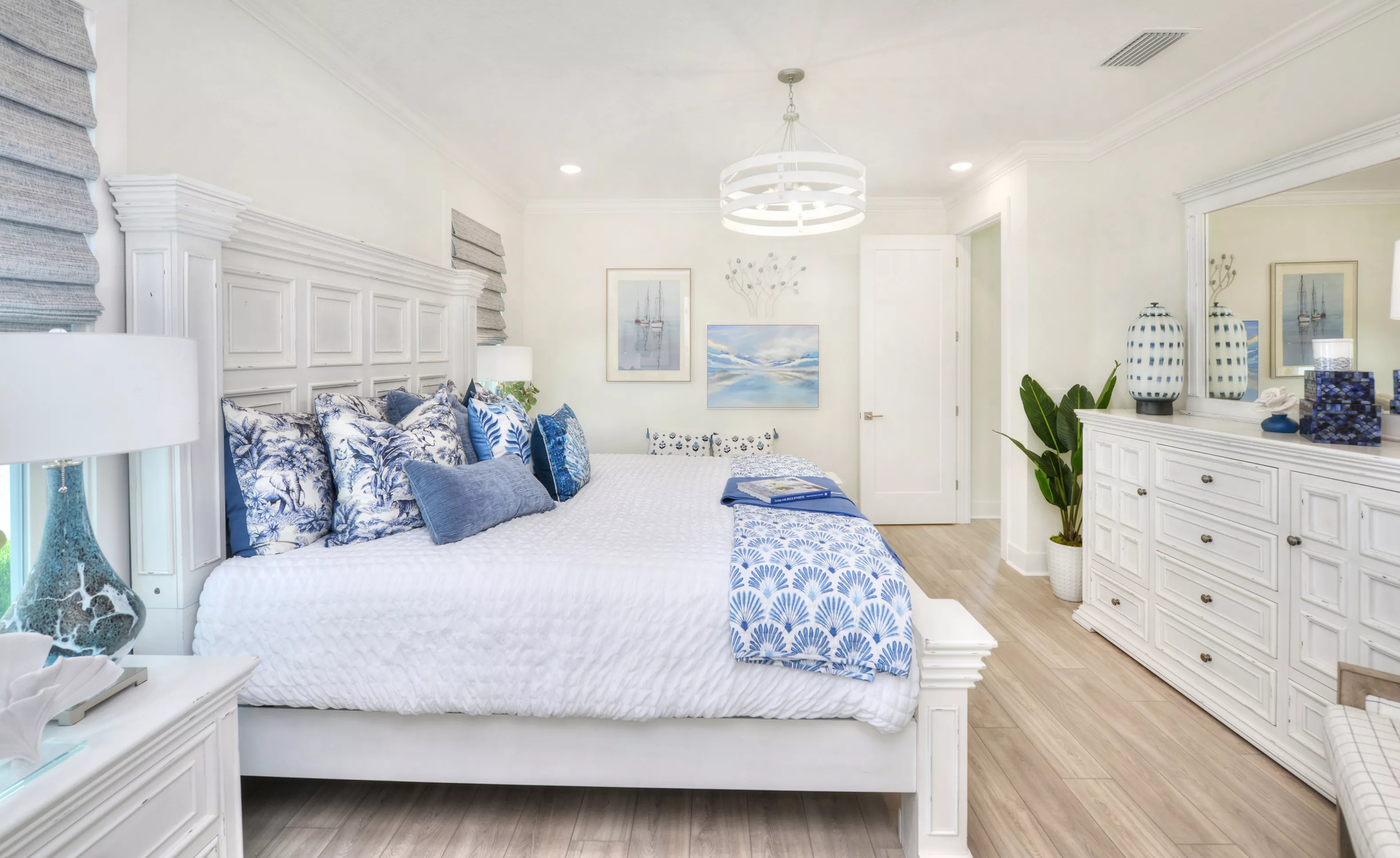 Primary bedroom with a white king bed, blue and white patterned pillows, white wood dresser, and wood-look plank flooring.