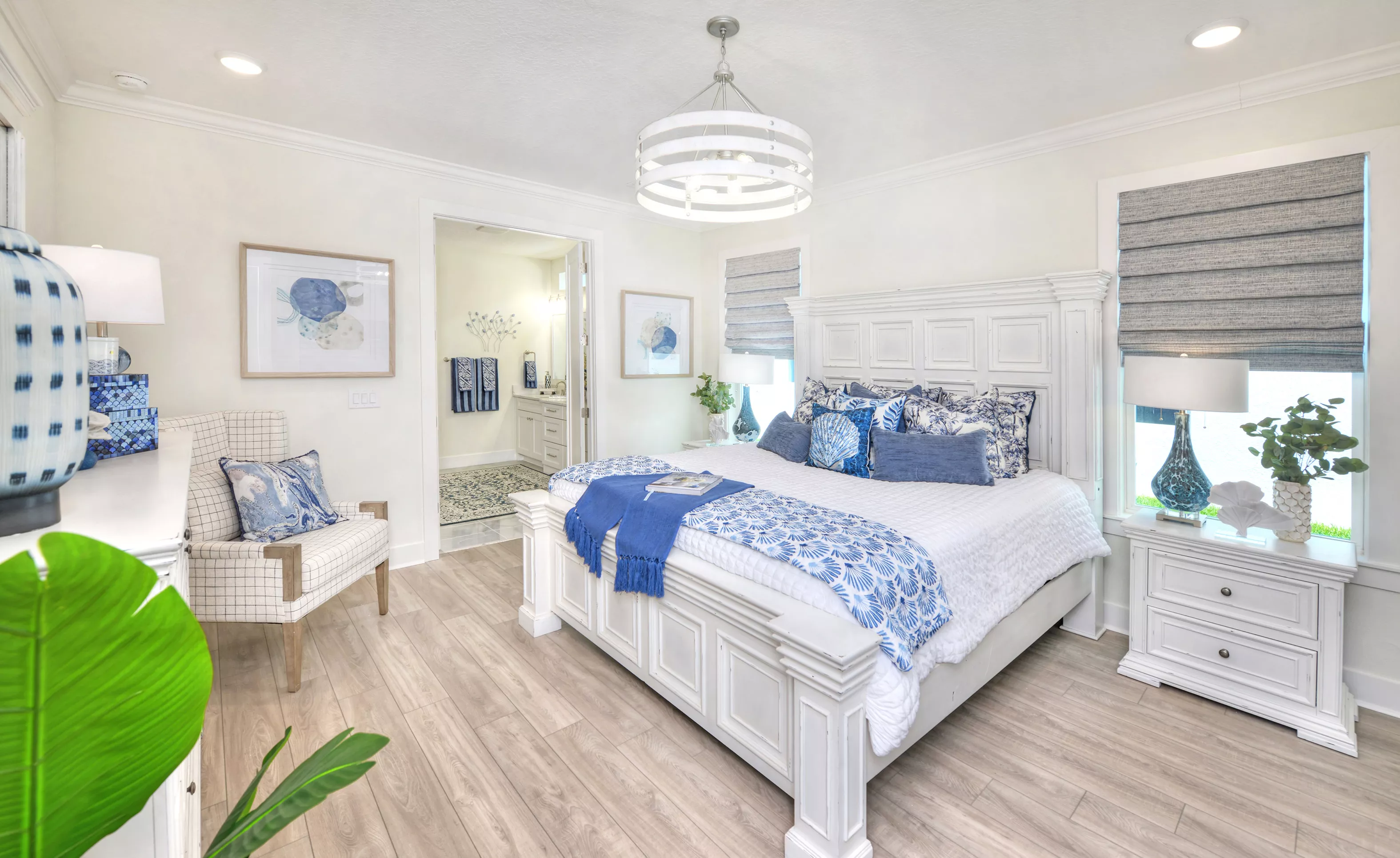 Primary bedroom in the Azalea plan with white bed frame, blue patterned bedding, wood-look flooring, and ensuite bathroom.