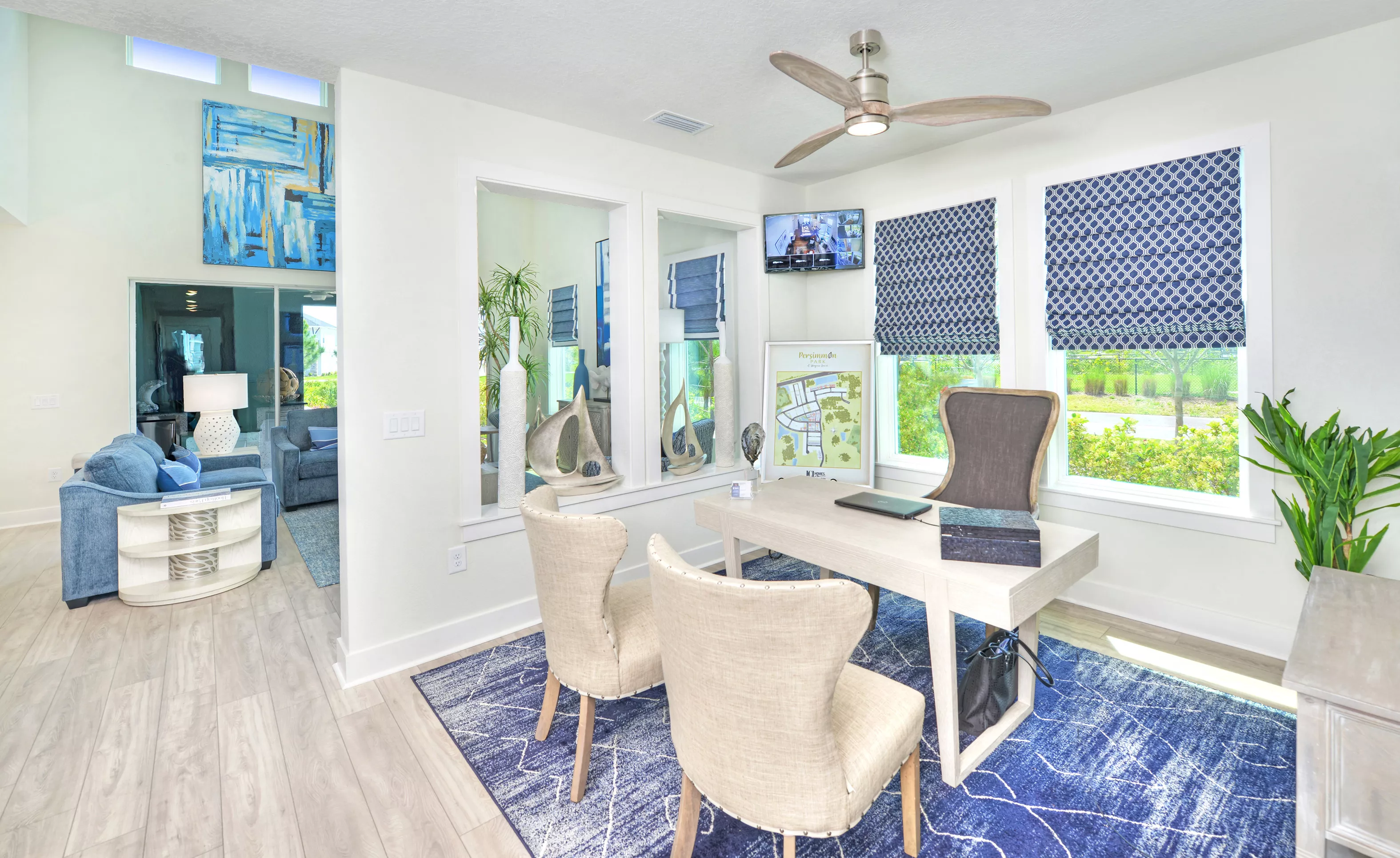 Azalea home office in Persimmon Park with a light wood desk, two upholstered chairs, a blue rug, and interior windows.