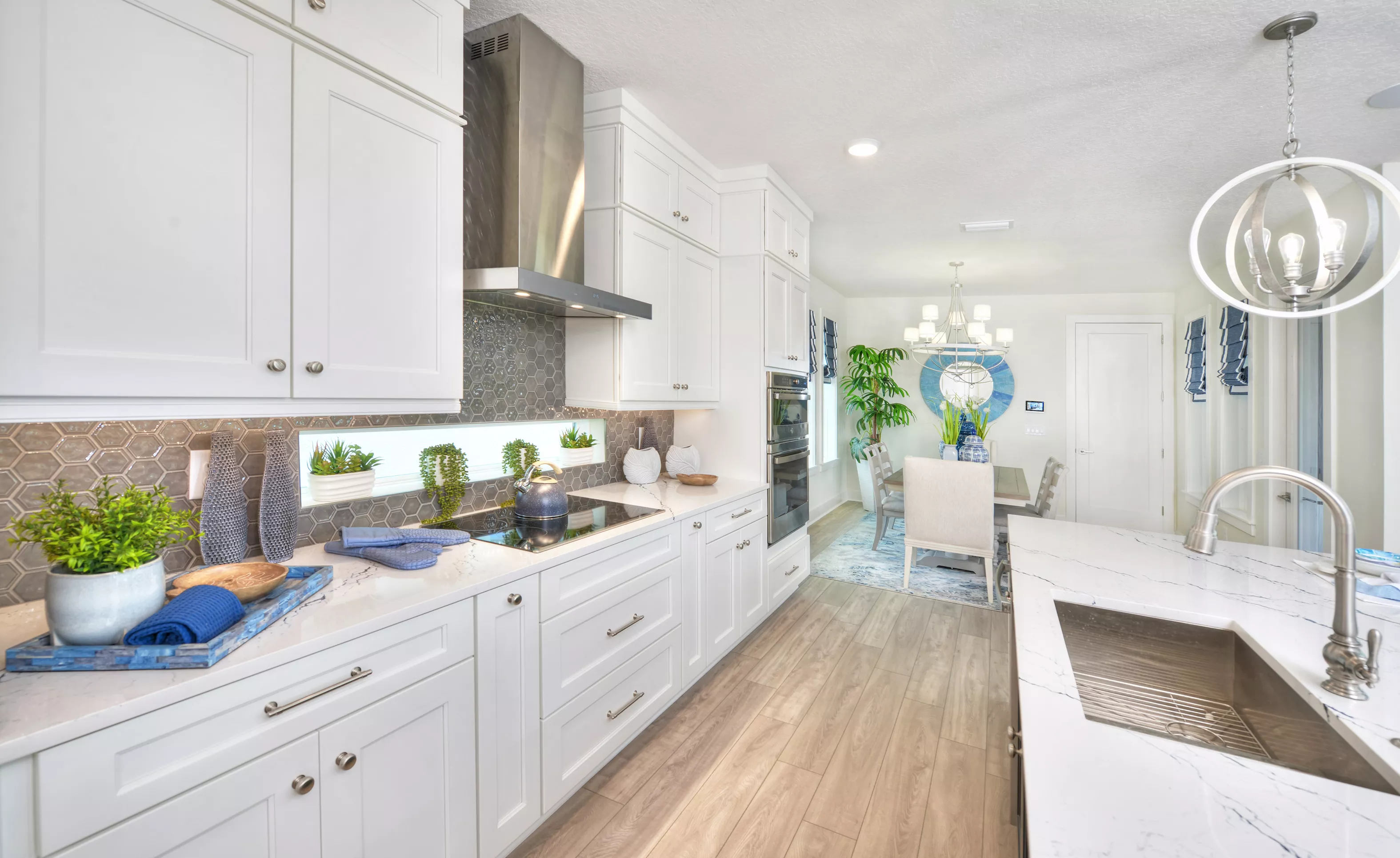 Azalea plan kitchen with white cabinets, gray hexagonal tile backsplash, stainless steel hood, and dining area beyond.