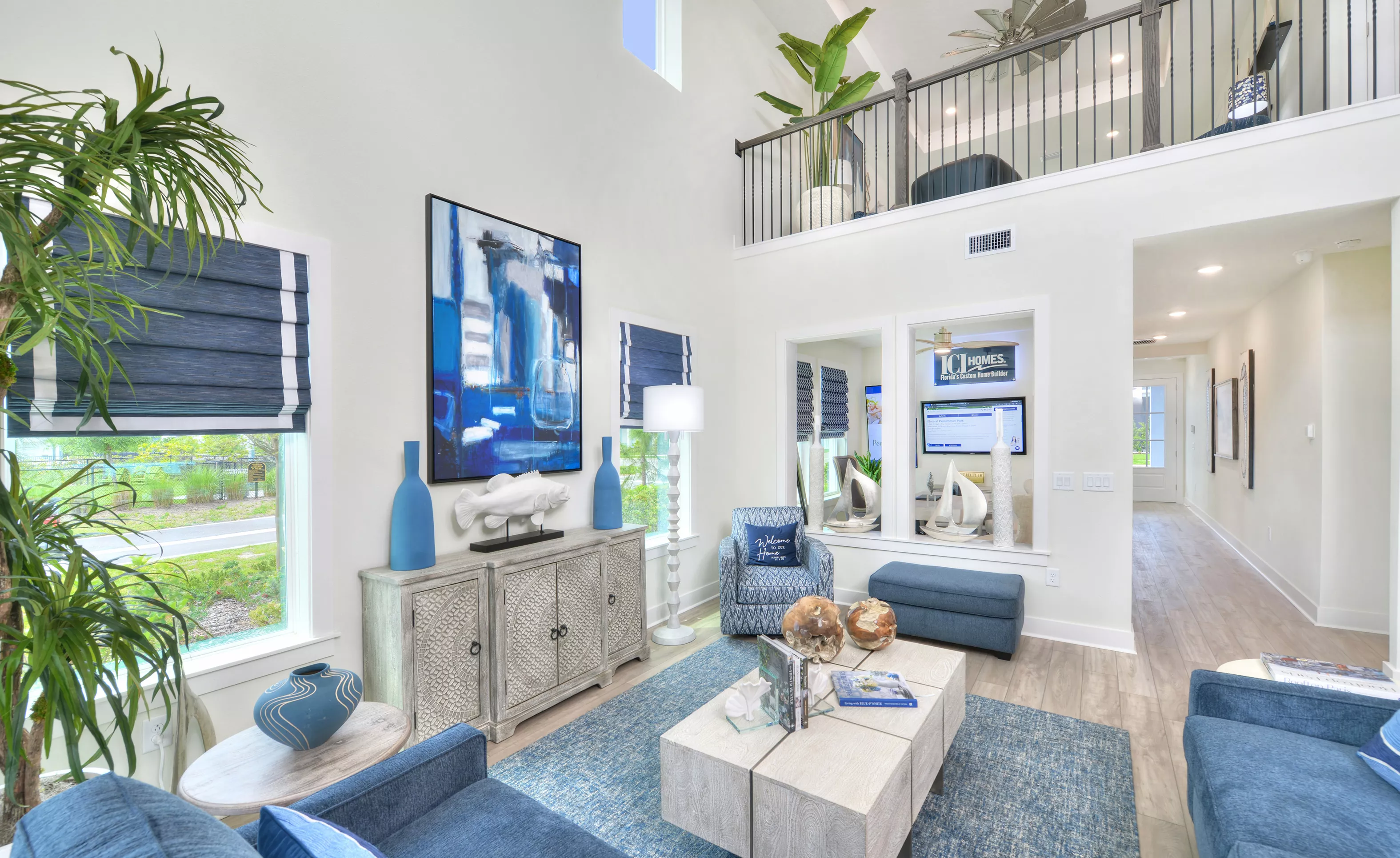 Two-story living room in the Azalea plan with a loft overlook, blue and white coastal decor, and large windows.