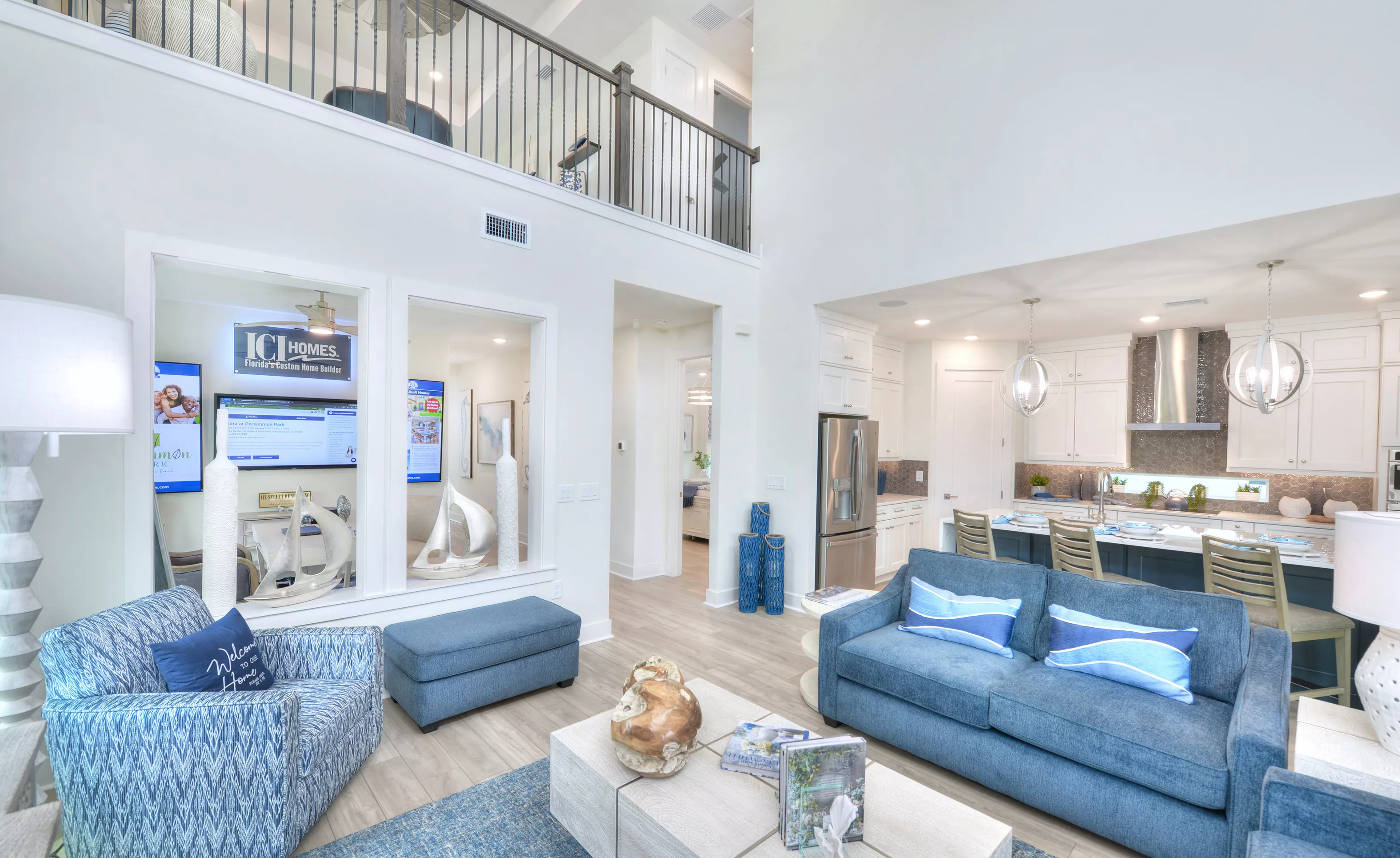 Living room of the Azalea plan with high ceilings, a balcony overlook, and a view into the kitchen with blue accents.