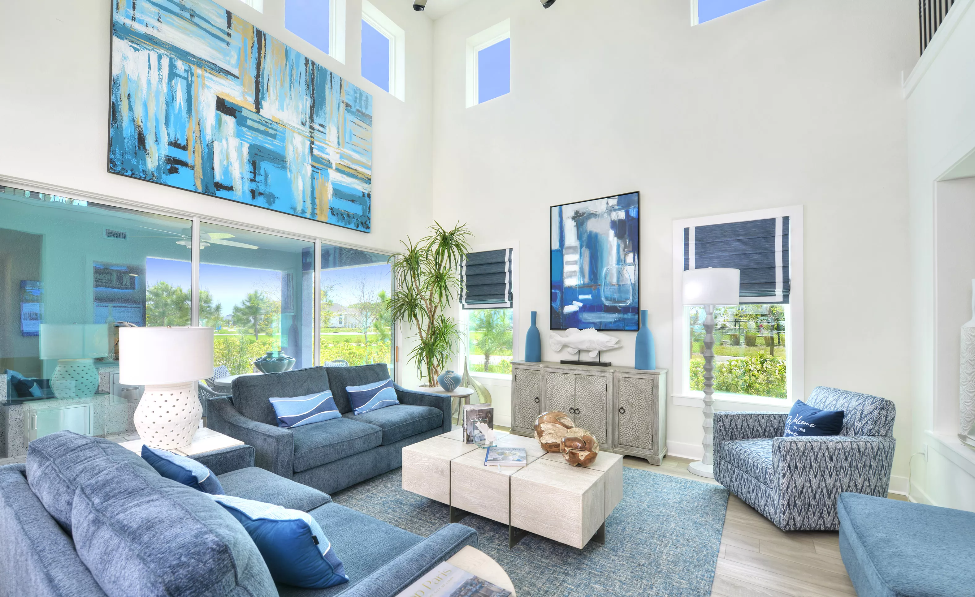 Azalea plan living room with soaring ceilings, tall windows, blue furniture, and large abstract wall art.