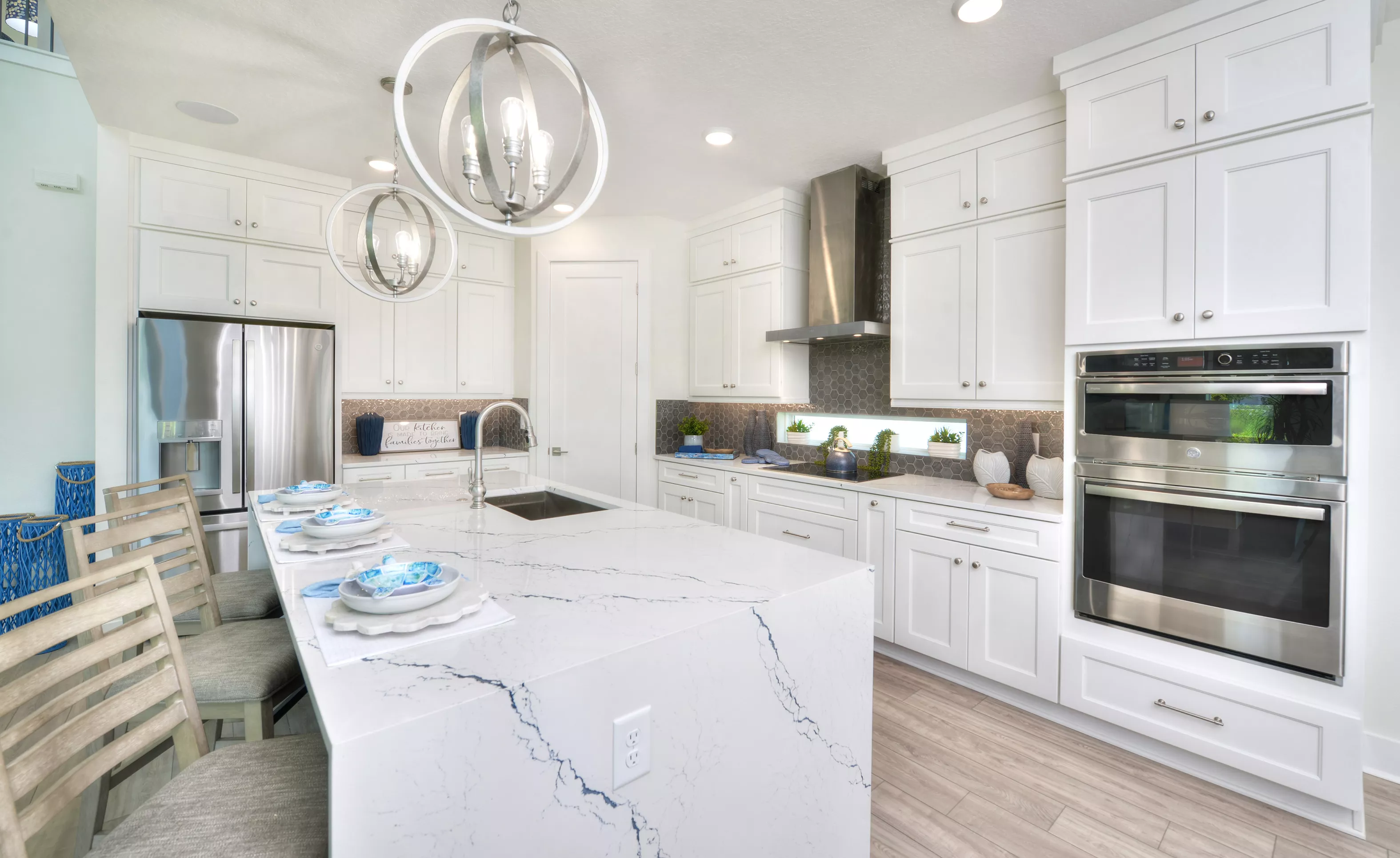 Kitchen of the Azalea plan with a marble-look island, white cabinets, stainless steel appliances, and orb pendant lights.
