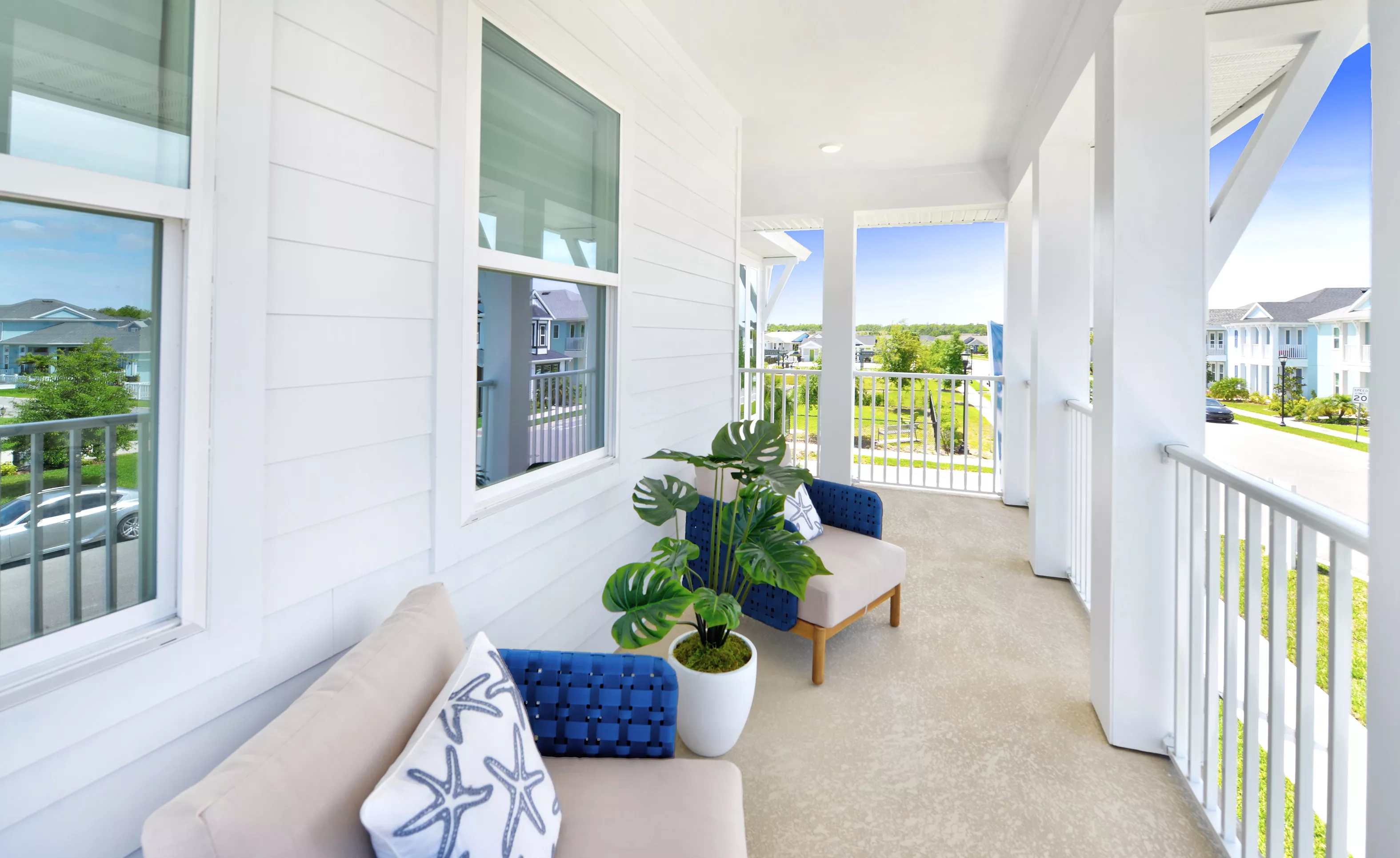 Covered porch of the Azalea plan at Persimmon Park, featuring white siding, a white railing, and two blue-accented chairs.