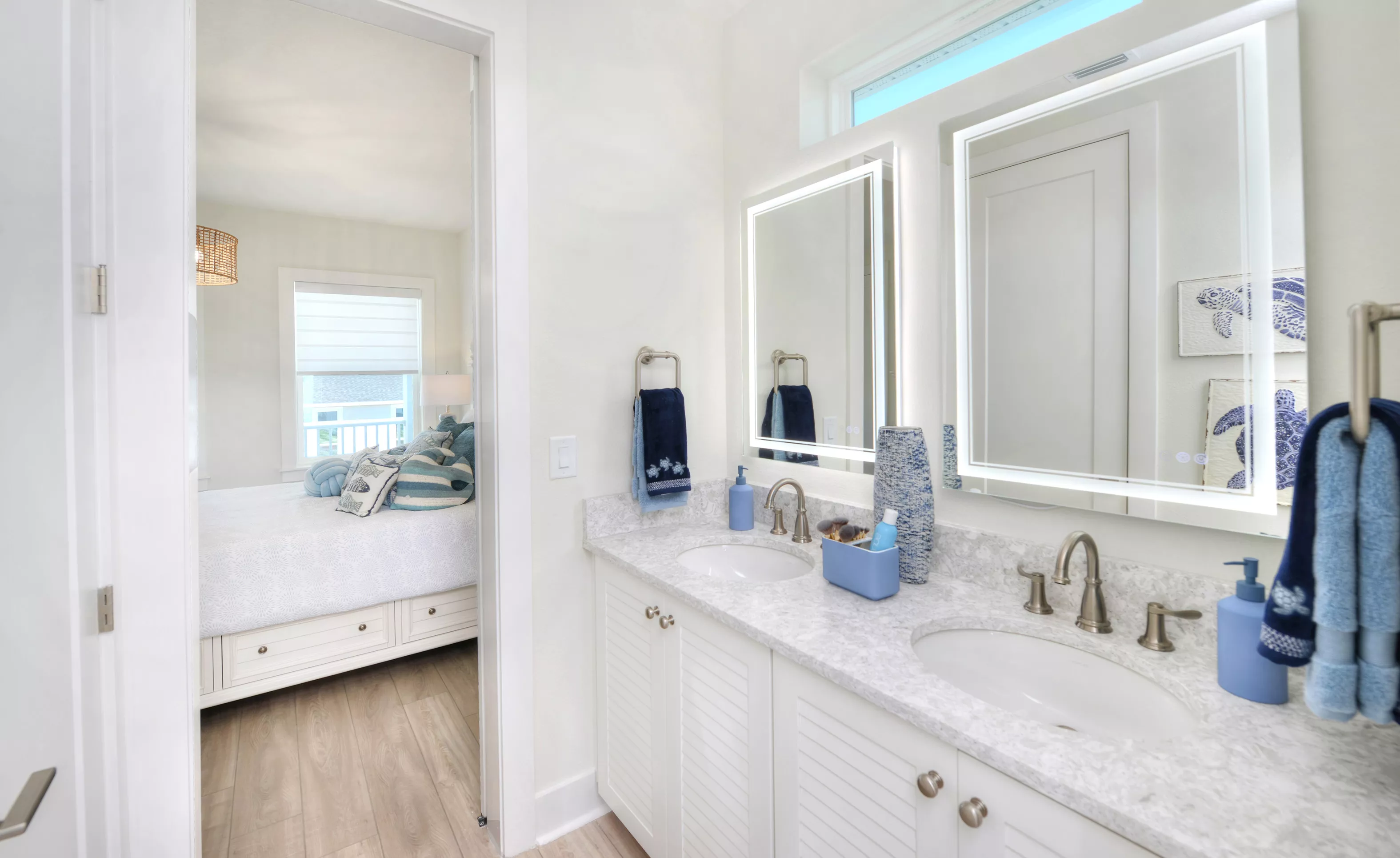 Primary bath with white double vanity, stone countertop, dual backlit mirrors, and view into a bedroom.