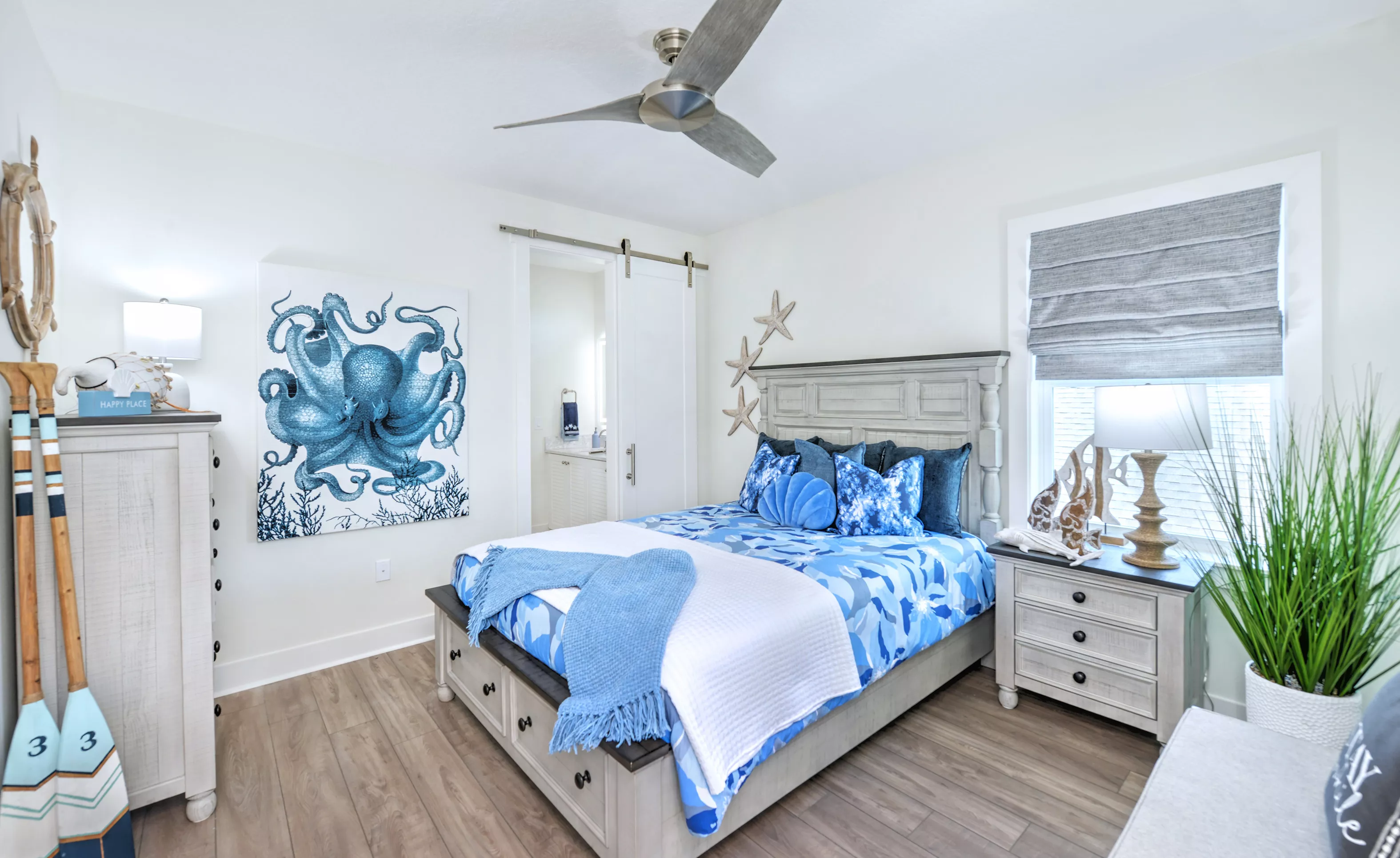 Secondary bedroom with wood-look flooring, a ceiling fan, and a white sliding barn door leading to an attached bathroom.