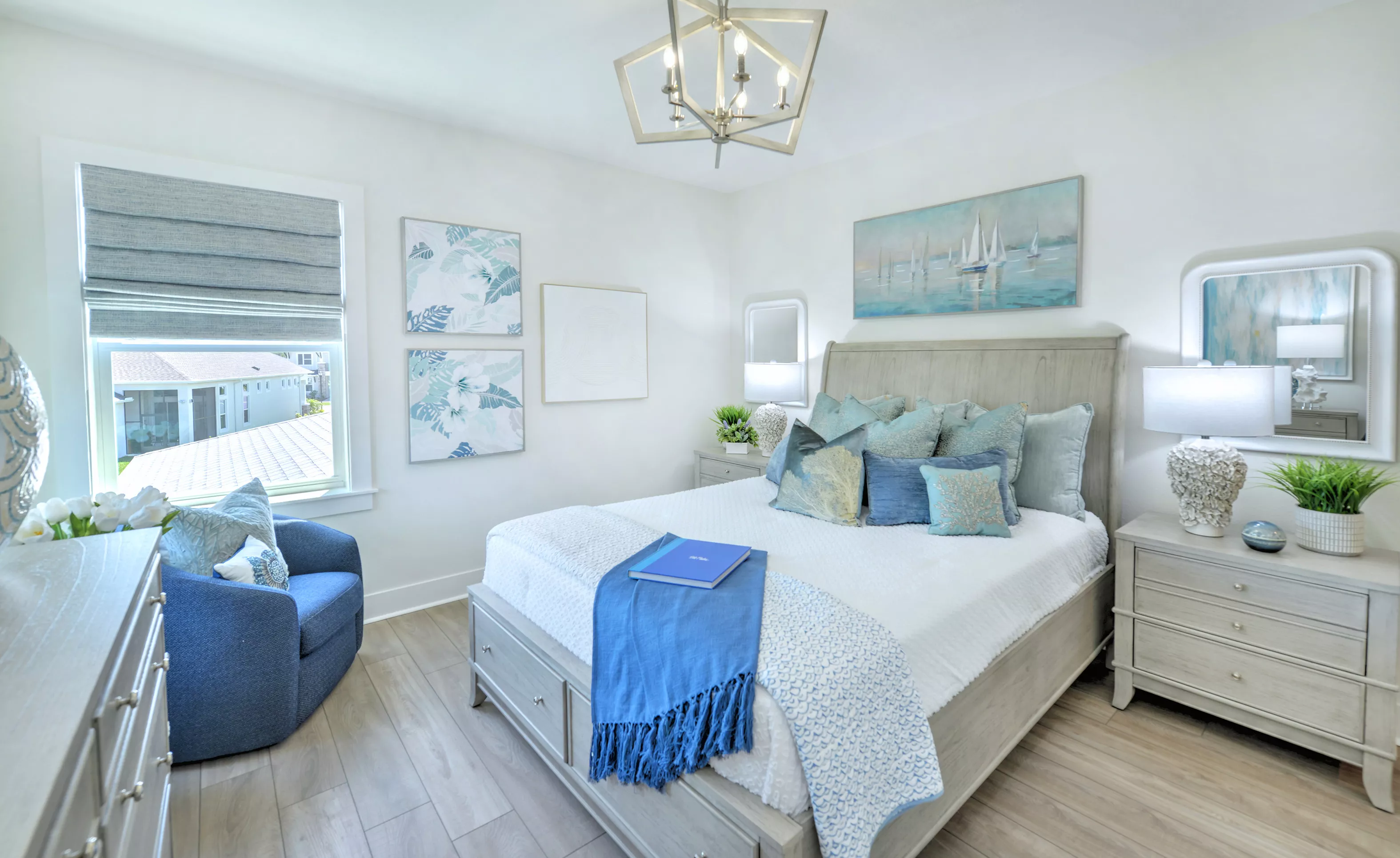Secondary bedroom in the Azalea plan featuring light wood-look flooring, a queen bed, blue accent chair, and chandelier.