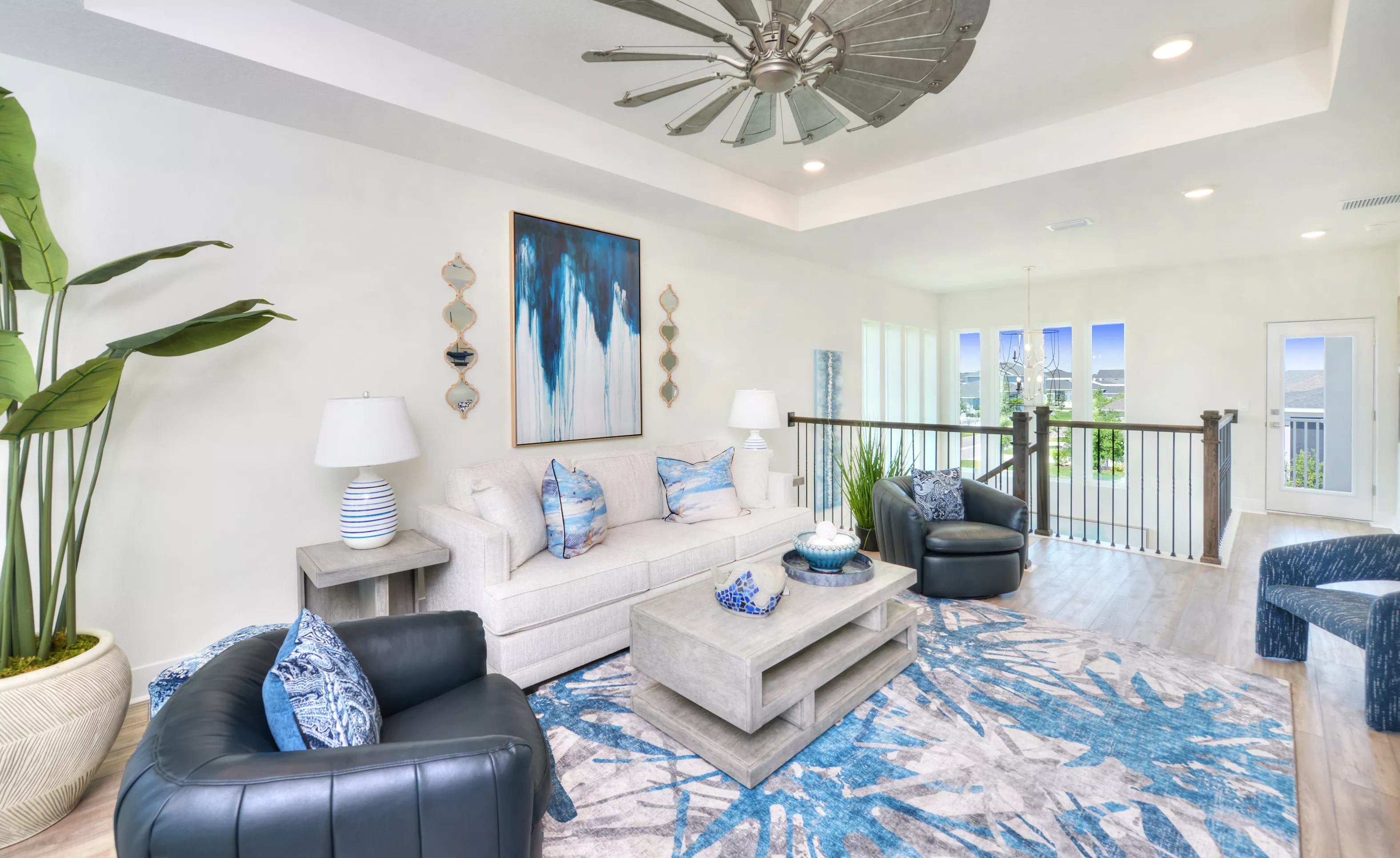 Bonus room in the Azalea plan with a tray ceiling, windmill ceiling fan, sofa, armchairs, and a blue-patterned area rug.