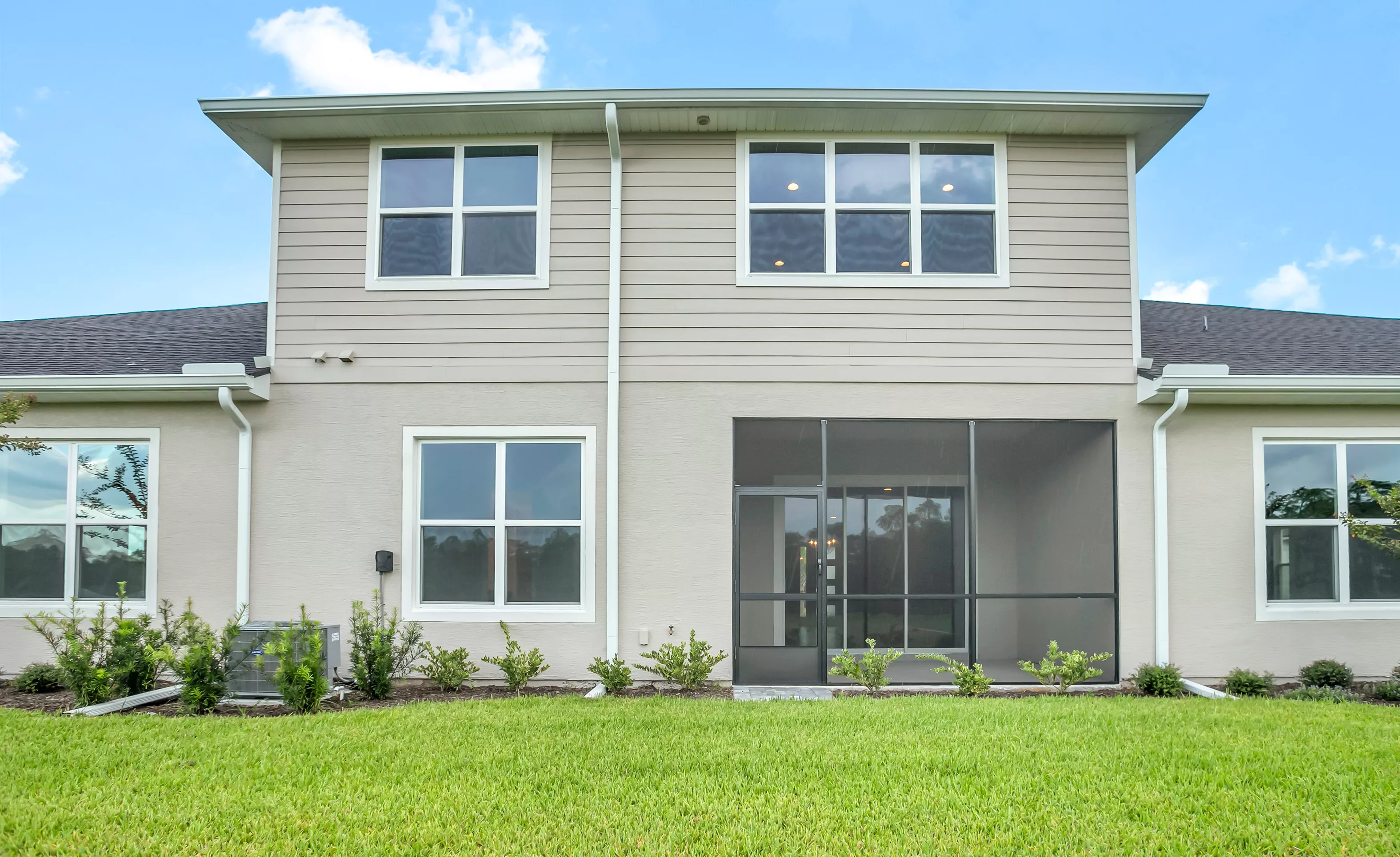 Rear exterior view of a two-story home with light siding, a screened-in back porch, and a landscaped yard.