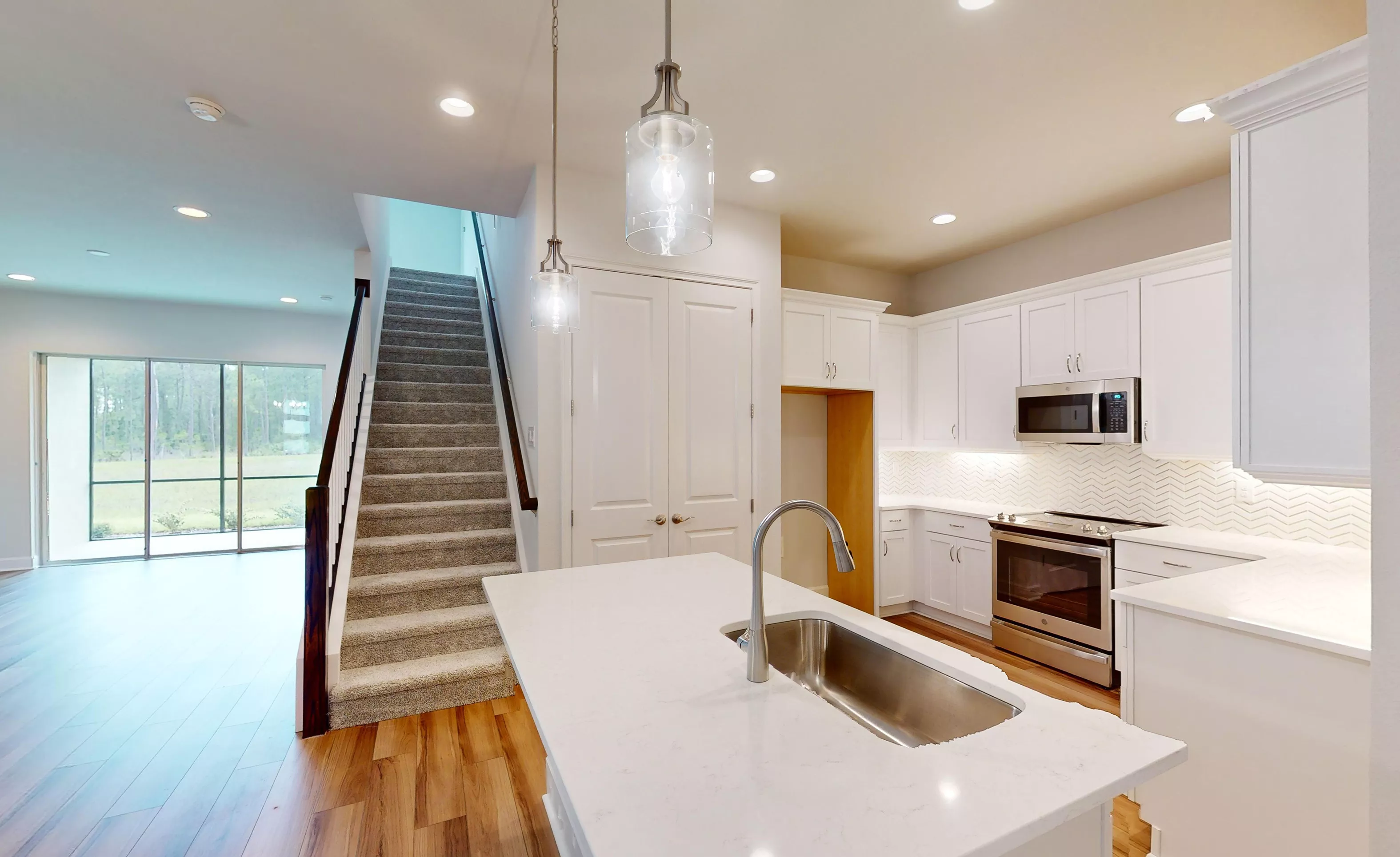 Kitchen of Blossom II plan with white cabinets, center island, stainless steel appliances, and a staircase.