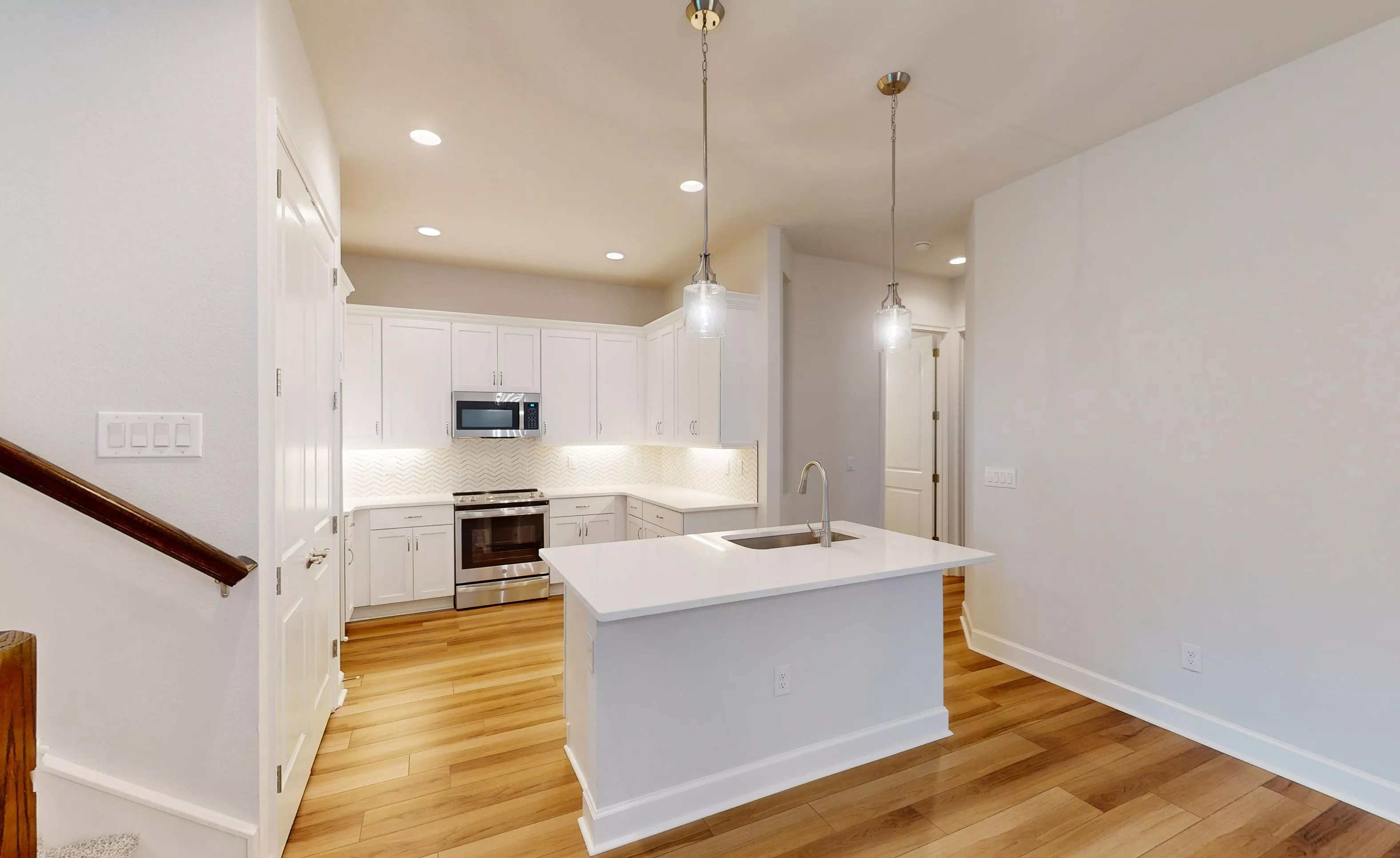 Blossom II kitchen with white cabinets, stainless steel appliances, herringbone backsplash, and a central island.