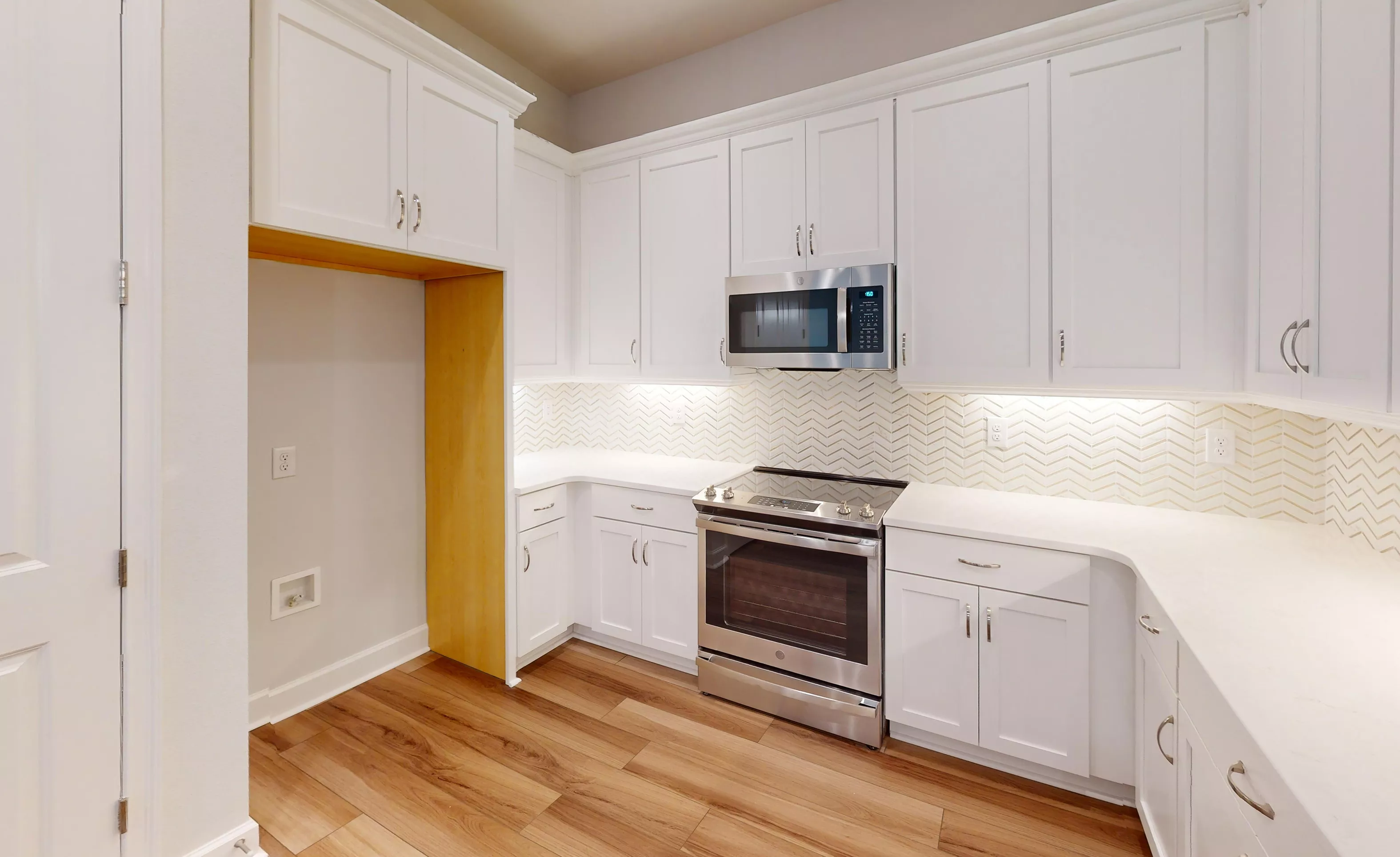 Blossom II kitchen with white cabinets, stainless steel appliances, light countertops, and herringbone tile backsplash.