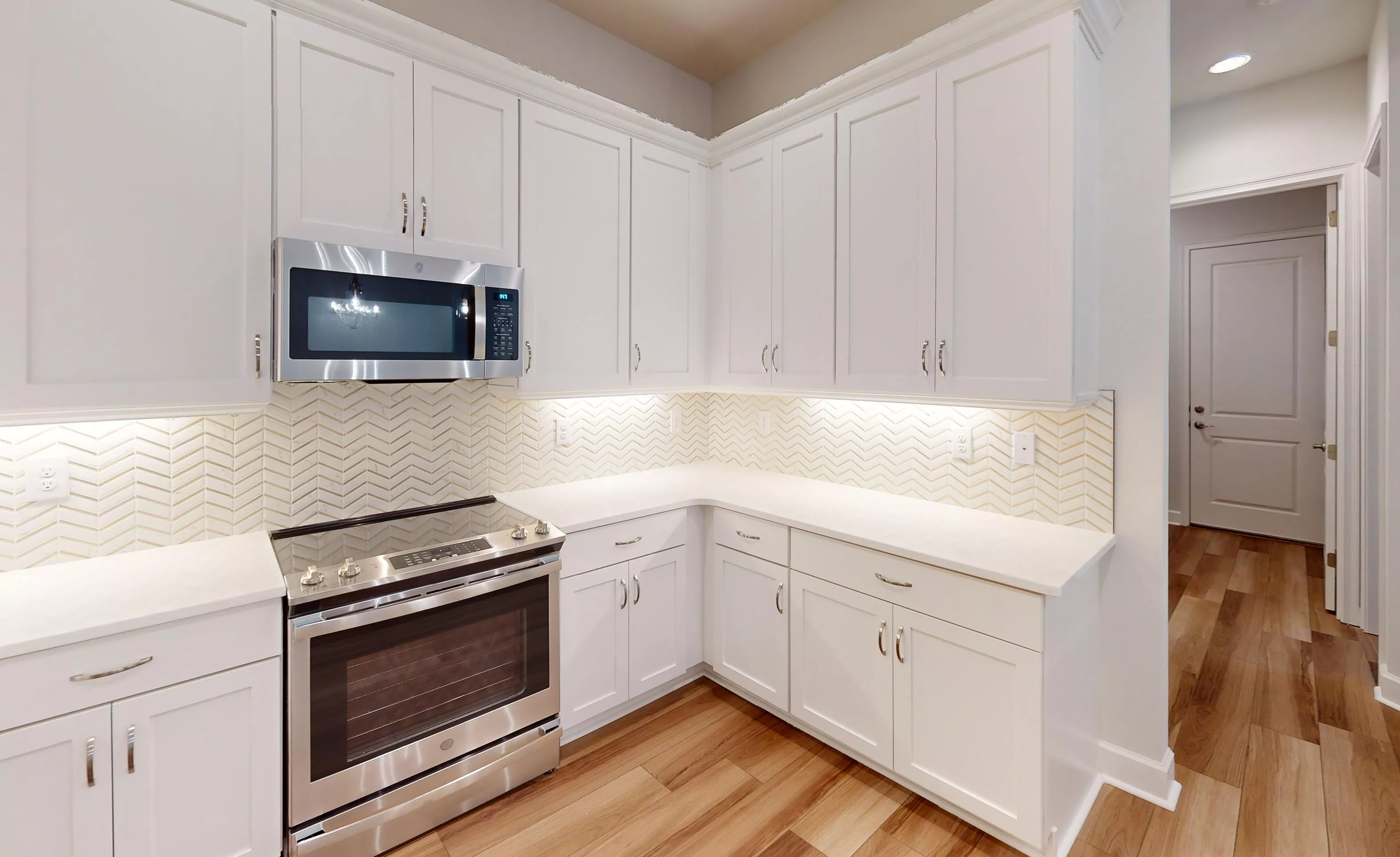 Kitchen of the Blossom II plan with white cabinetry, stainless steel appliances, and a light herringbone tile backsplash.